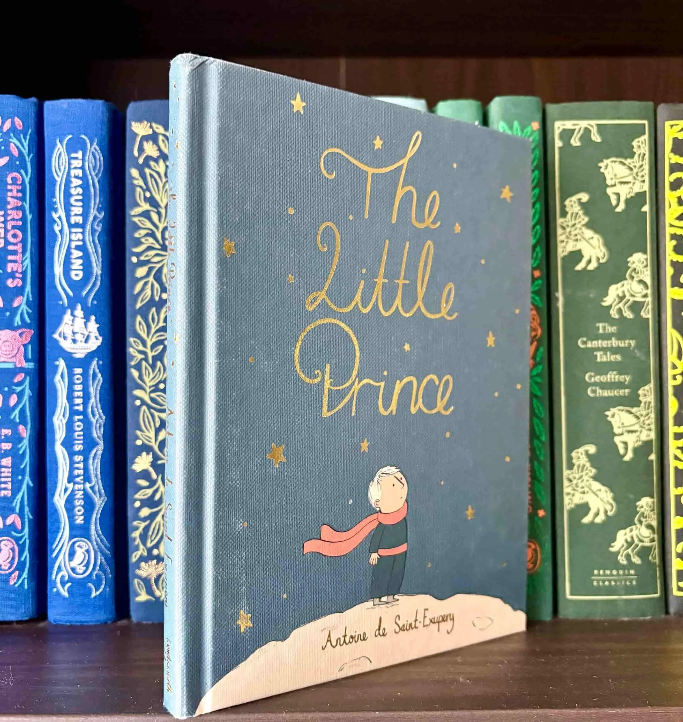 Cover of The Little Prince book on a bookshelf, showing the little prince starting at the stars illustration.