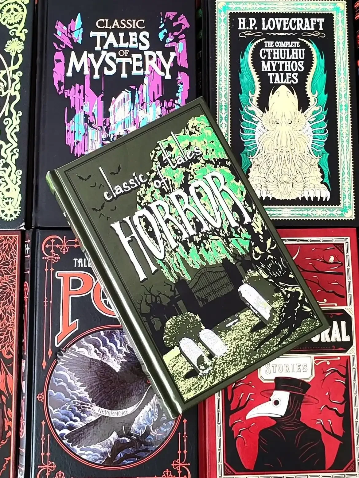 A green leatherbound edition of Classic Tales of Horror, featuring gravestones and a cemetery, laying on top of 4 other classic horror books 2026