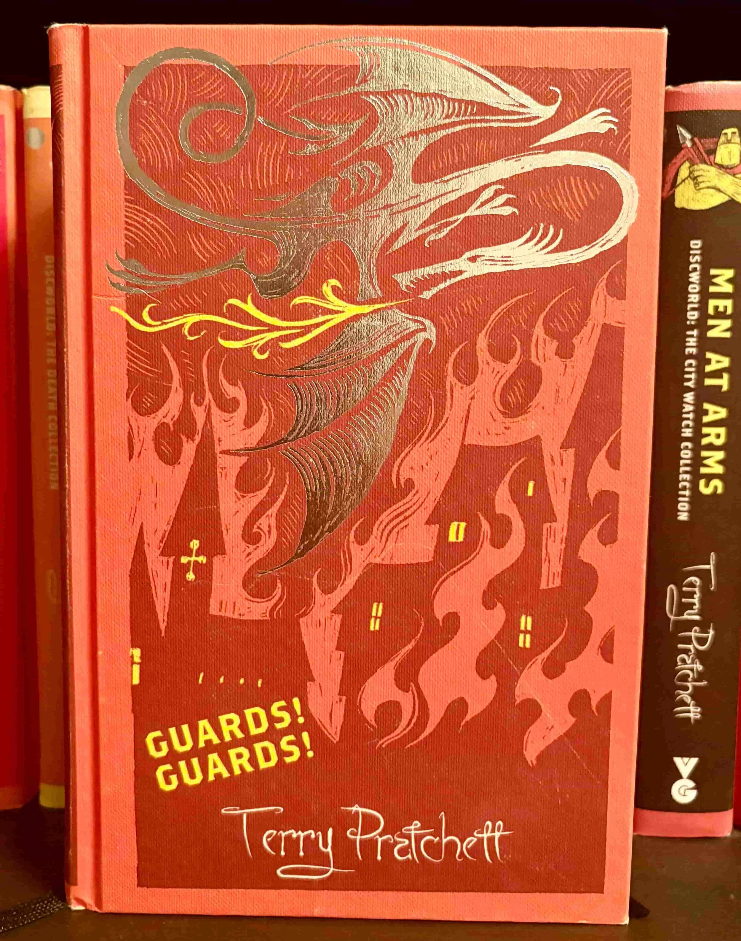 The red cloth cover of Guards! Guards! by Terry Pratchett, featuring a stylized dragon silhouette over a city.