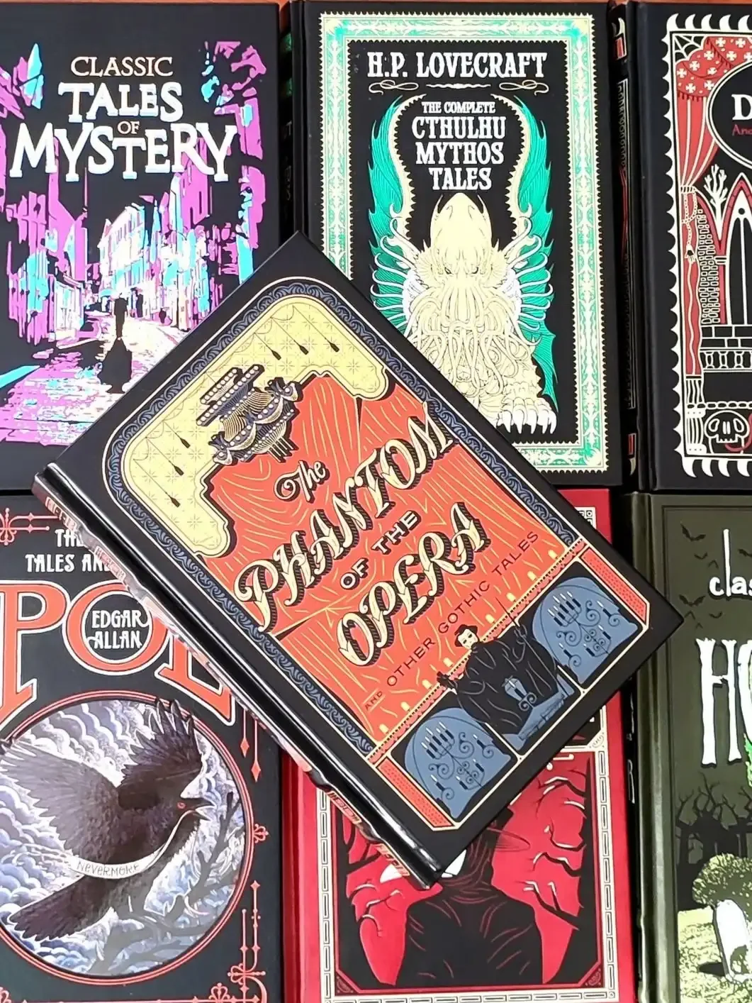 Red, black, and yellow leatherbound edition of The Phanto of the Opera, featuring the Phantom at the bottom of the cover, laying on top of 6 other classic horror books