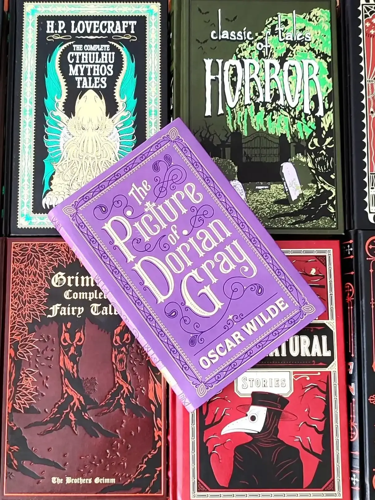 A purple flexibound edition of The Picture of Dorian Gray by Oscar Wilde laying on top of 4 other classic horror novels
