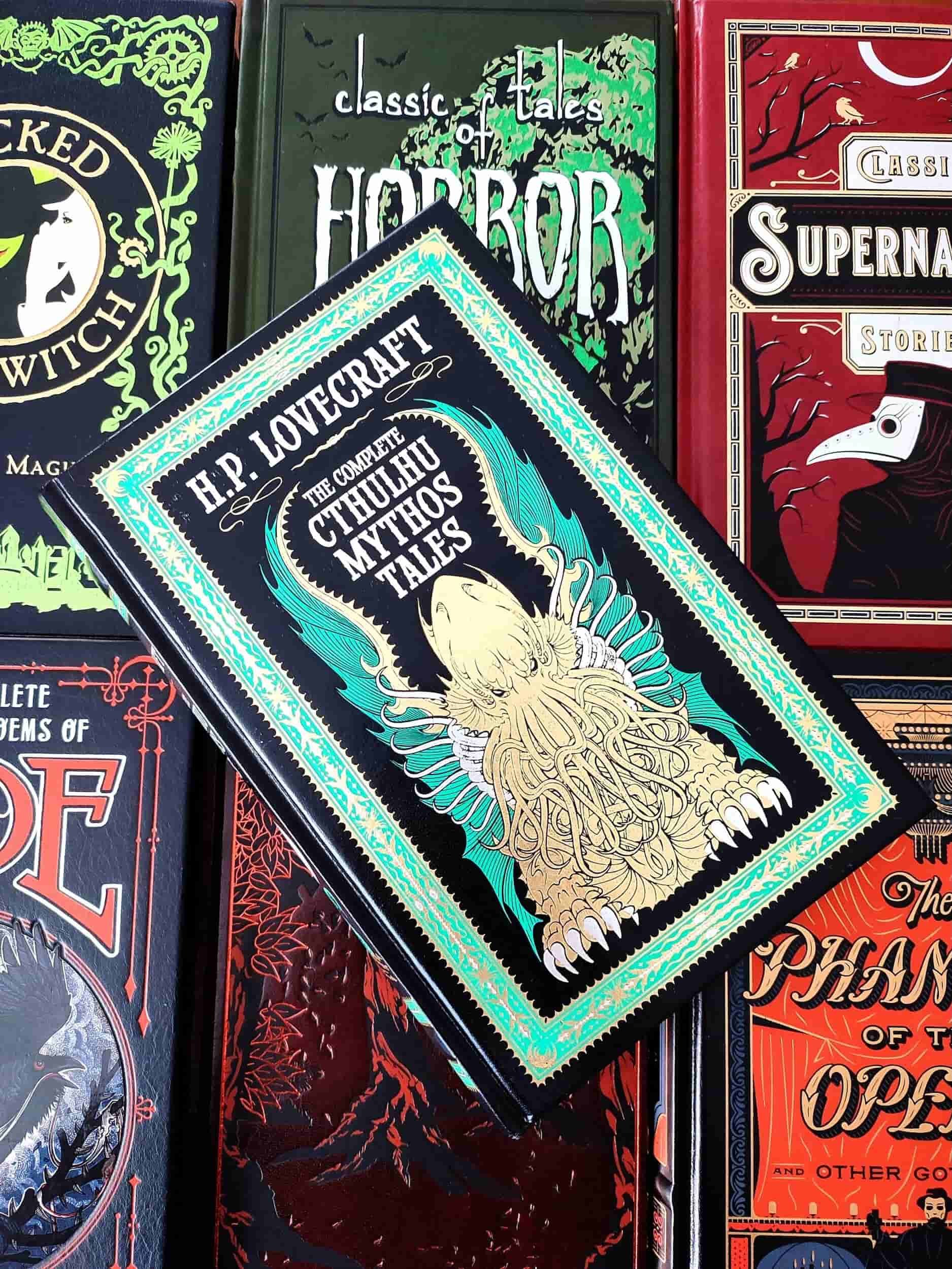 Leatherbound edition of The Complete Cthulhu Mythos Tales by H. P. Lovecraft, featuring a yellow and green design of Cthulhu and green edges with runes on the front cover. Laying on top of 6 other classic horror books.