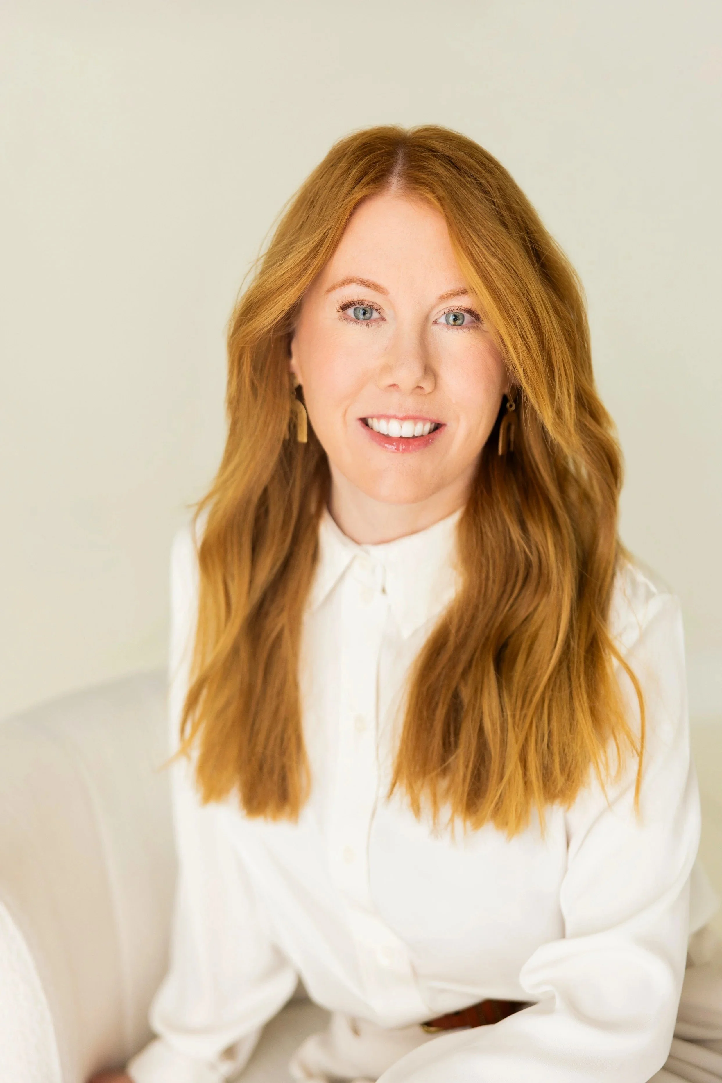 Portrait of a Jen Adkins, wearing a white blouse, smiling against a plain light-colored background.