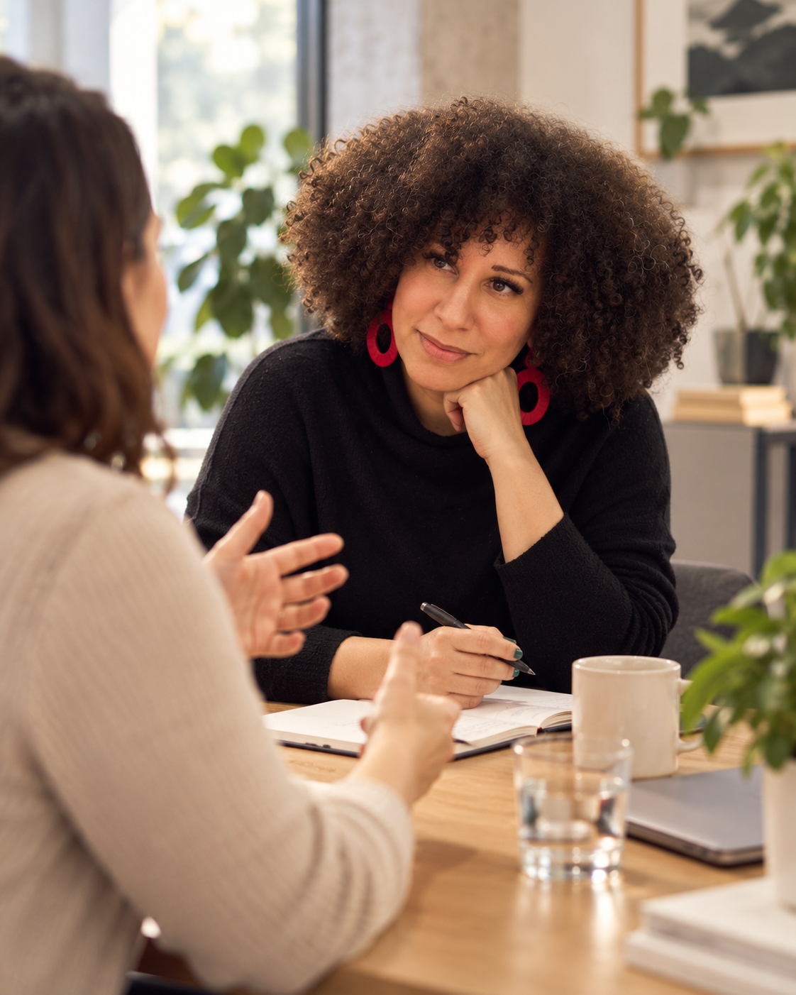 woman with curly hair in professional attire with red earrings talking to a client across a table