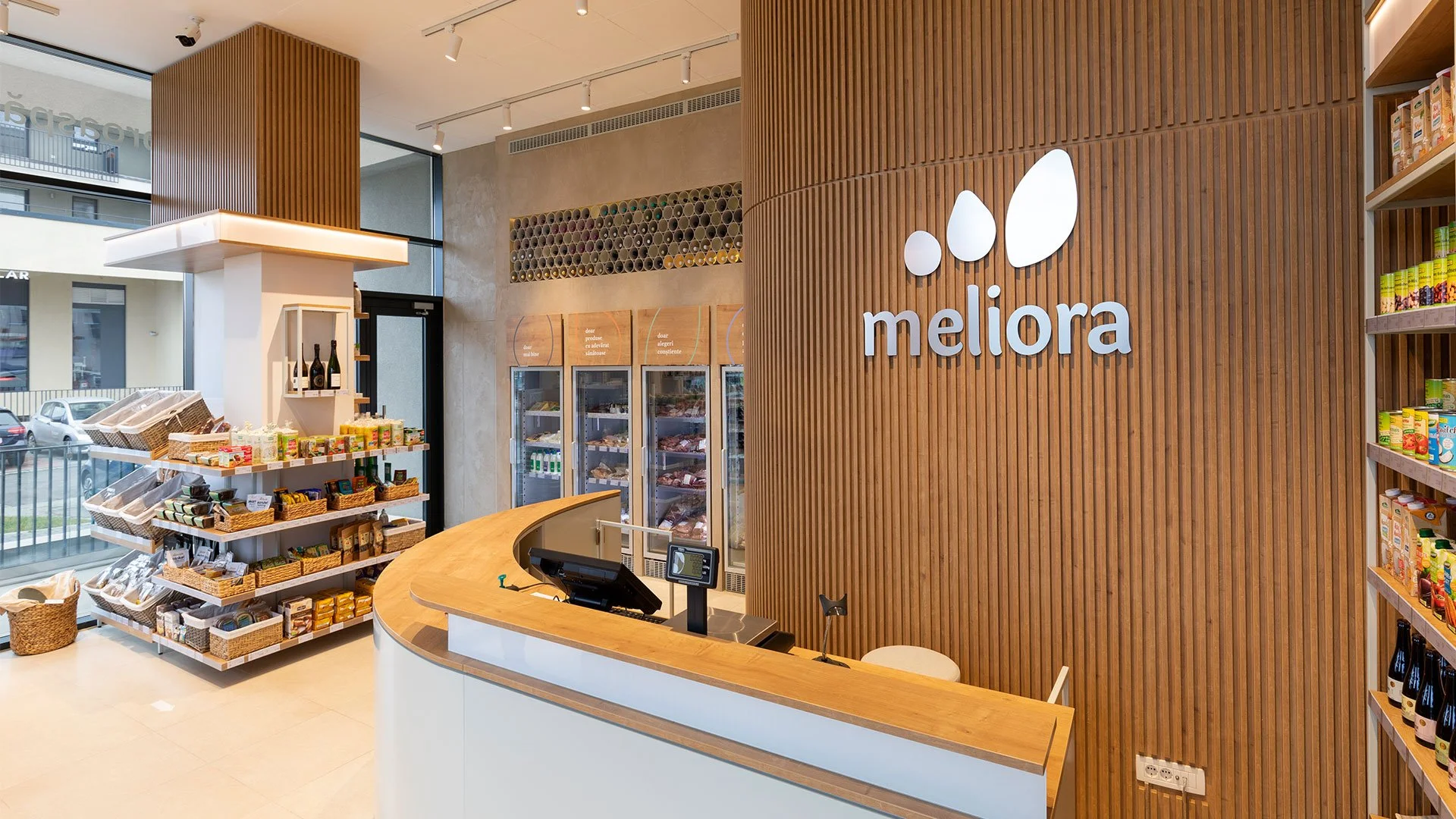 Meliora store interior featuring the logo on a wooden slat wall, a curved checkout counter and shelves with health food products.