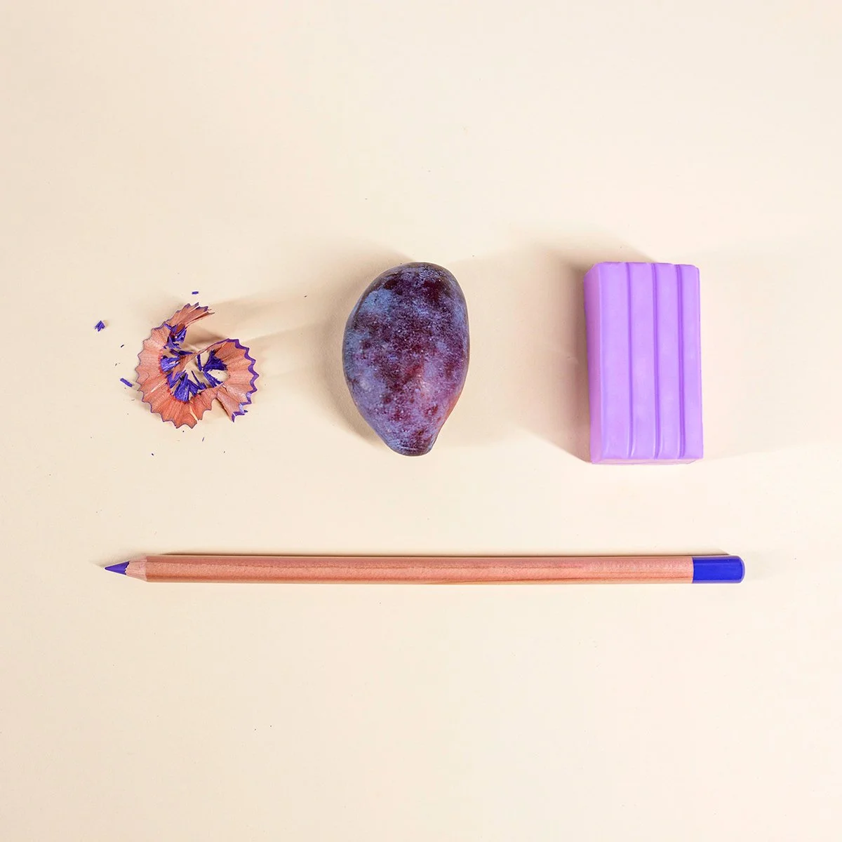 A plum, a pencil and purple sculptural objects arranged on a peach background as part of Plumline's brand imagery.
