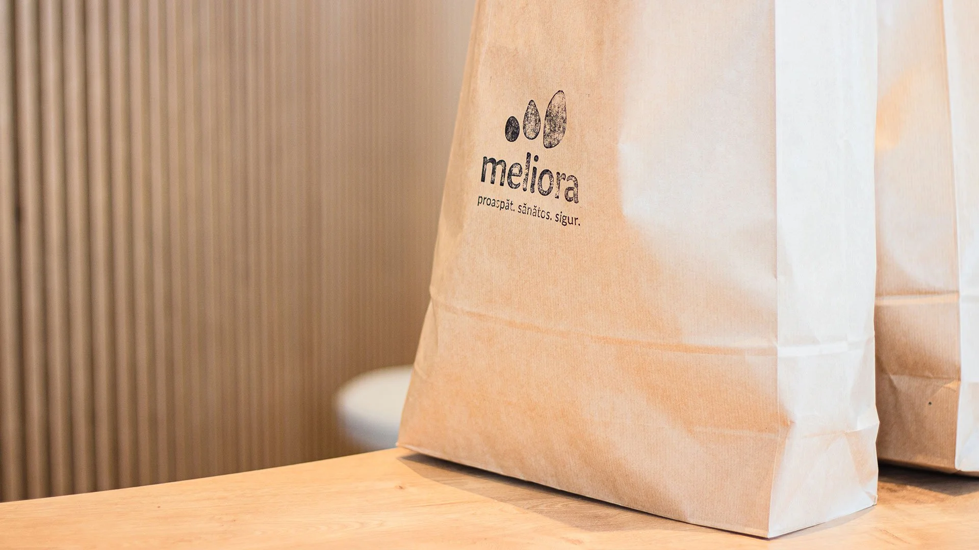 Meliora health food store logo printed on a kraft paper bag against a natural wood backdrop.