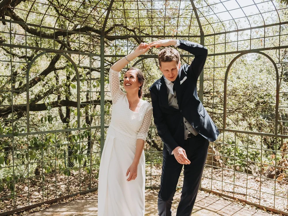 A bride and groom dancing outside under a metal gazebo surrounded by trees.