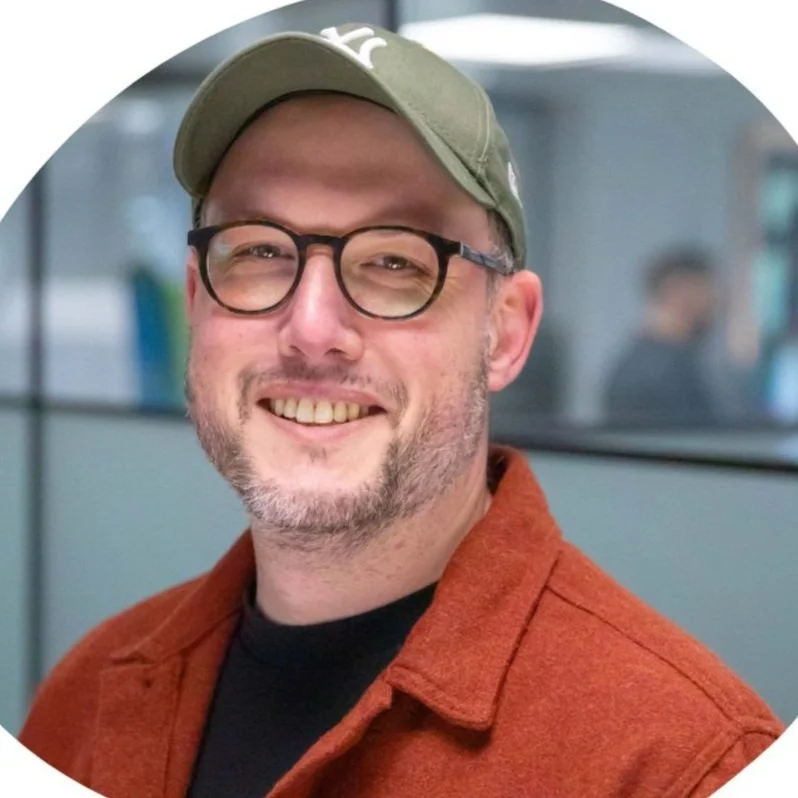 Person wearing glasses and a green cap indoors