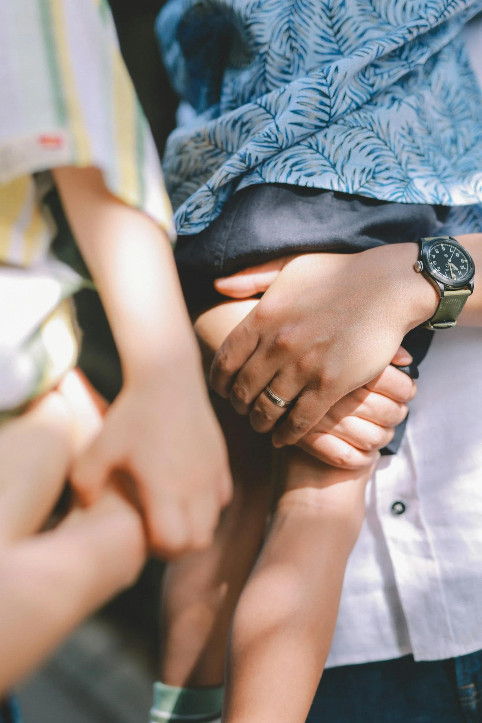 Multiple people holding hands, including a child, an adult, and a person wearing a watch, with a dog resting on the person's lap.