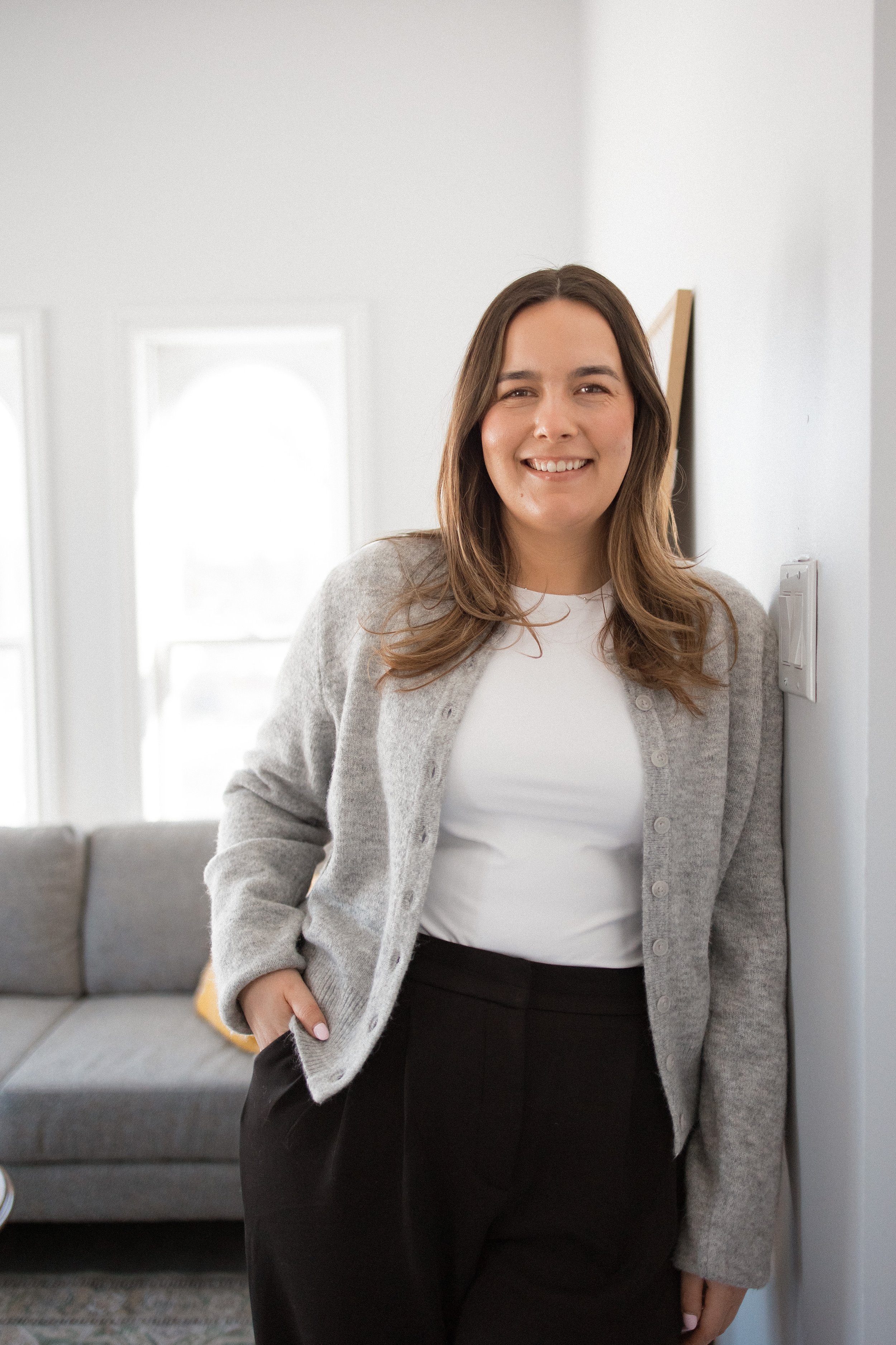 Person smiling with wavy hair and wearing a black sweater against a light background.
