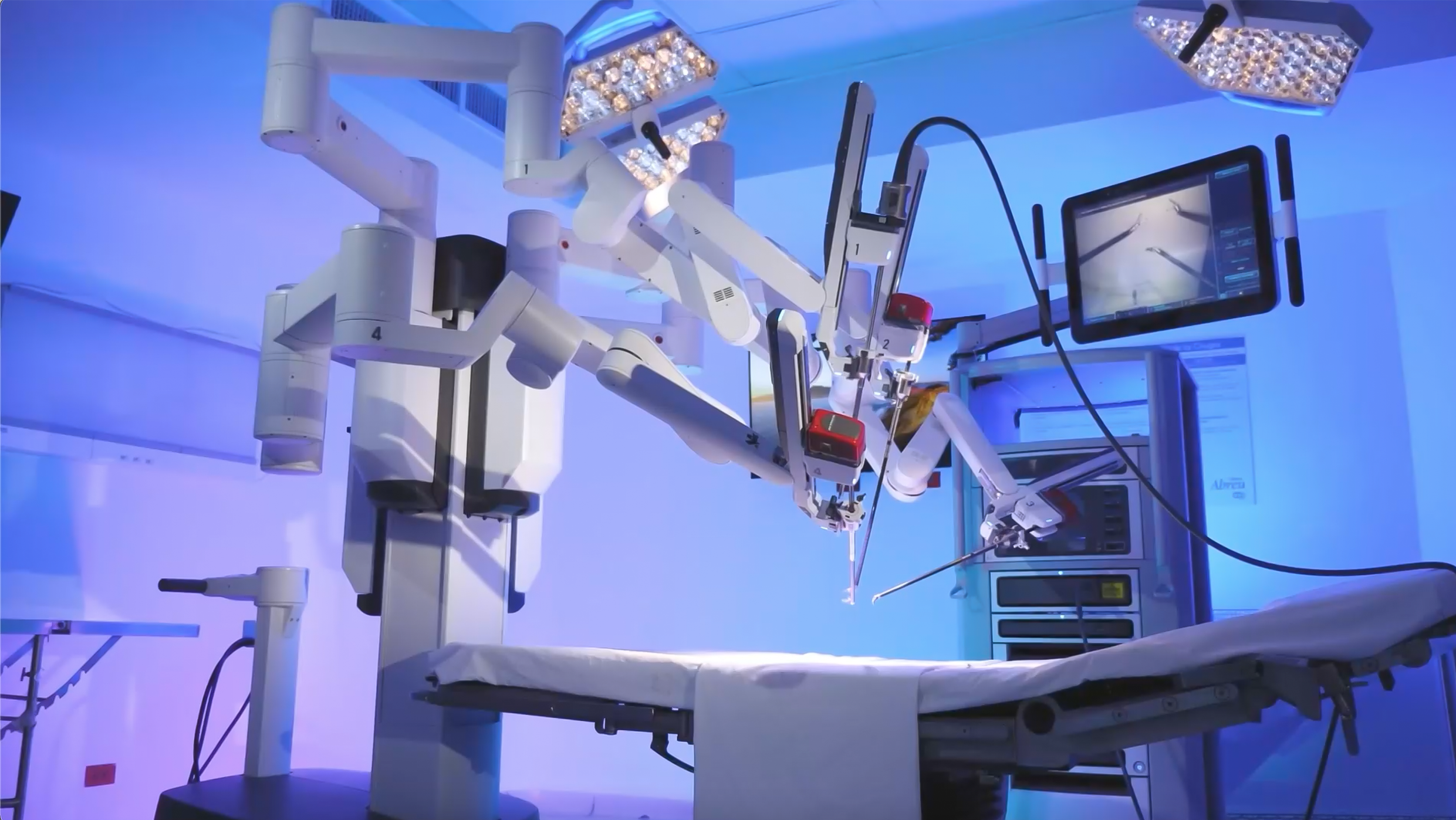 Robot quirúrgico en un quirófano moderno con iluminación azulada, equipado con múltiples brazos articulados y una pantalla de monitoreo.
