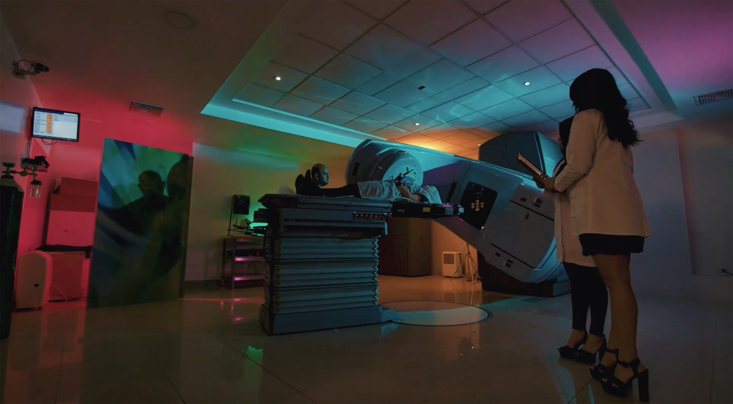 Paciente recibiendo una tomografía en un equipo de diagnóstico. Persona con bata médica, mujer, acudiendo con una profesional en un entorno clínico de luces suaves y colores vibrantes.