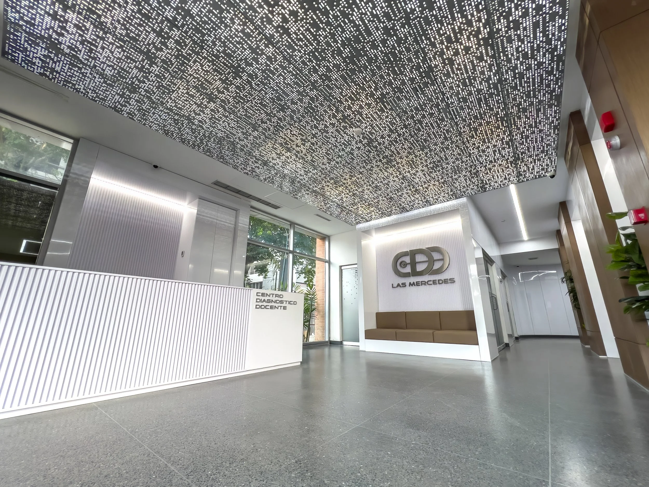 Vestíbulo de un edificio moderno con muro de recepción blanco, sillones negros, señalizada como 'Centro Diagnóstico Docente', y una pared con logo de Mercedes Benz.