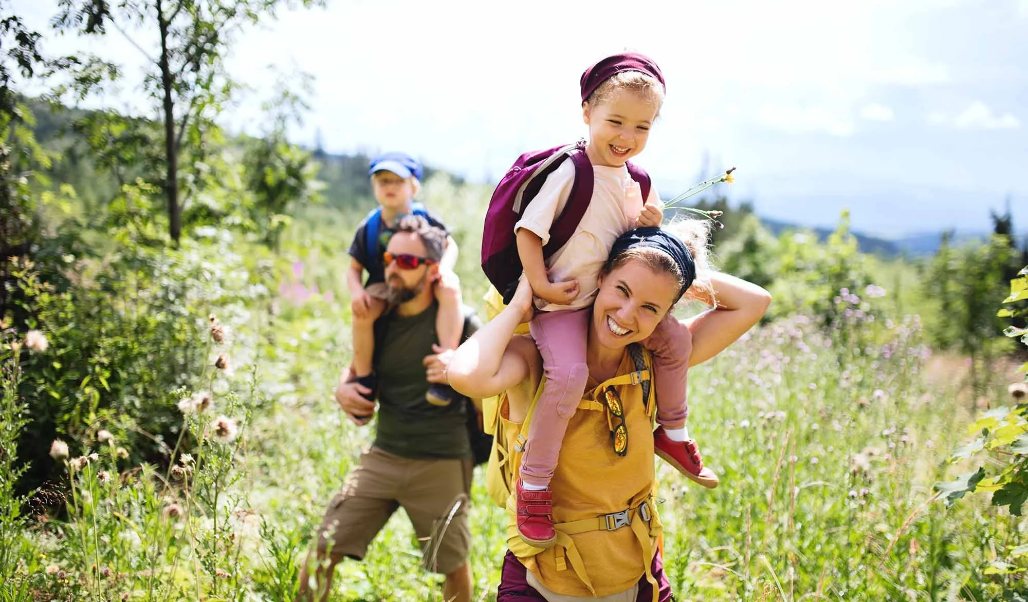 Family hiking in Kalispell, Montana with small girl on mom's shoulders, father and son in background
