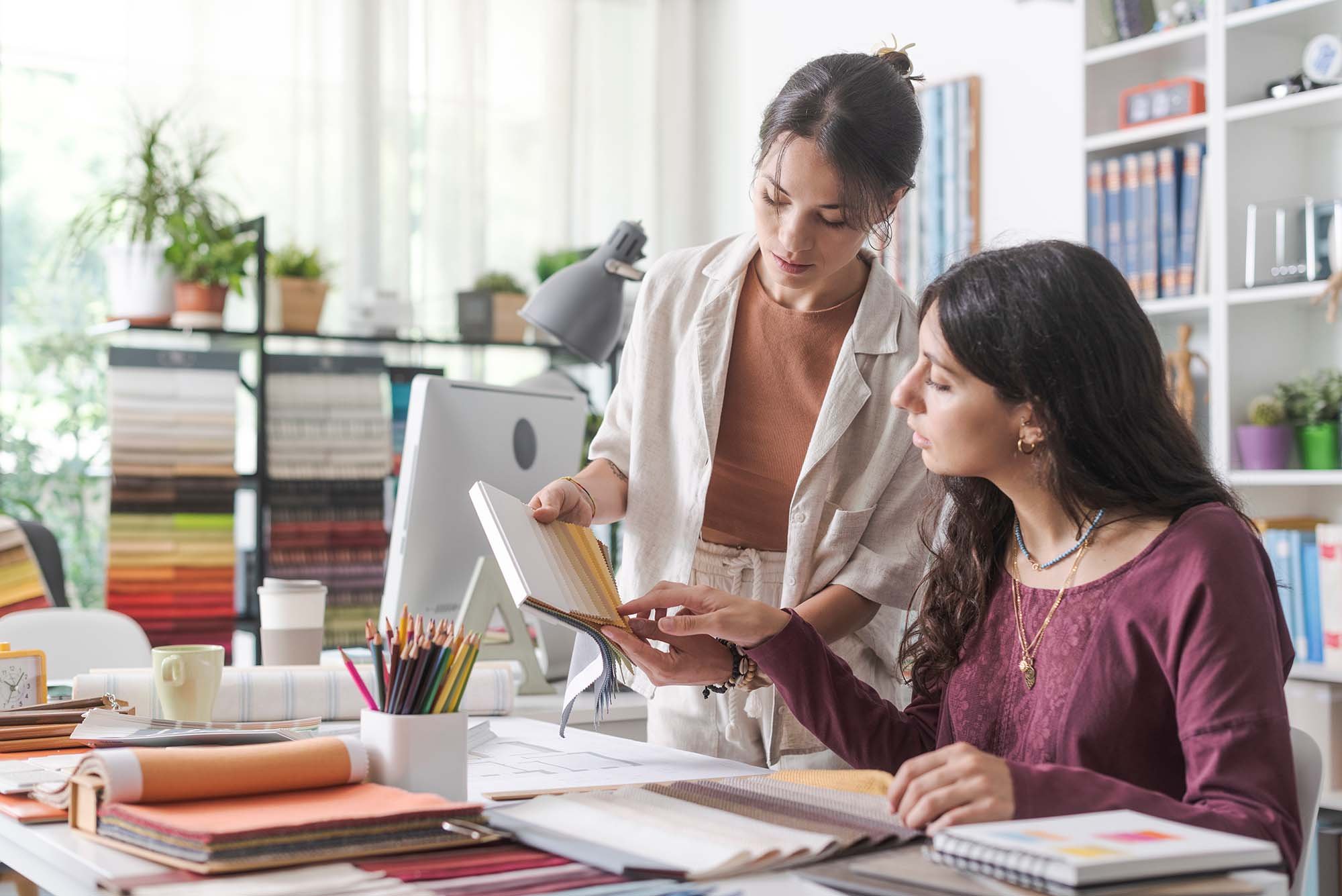 Two women sitting at a desk viewing color swatches together