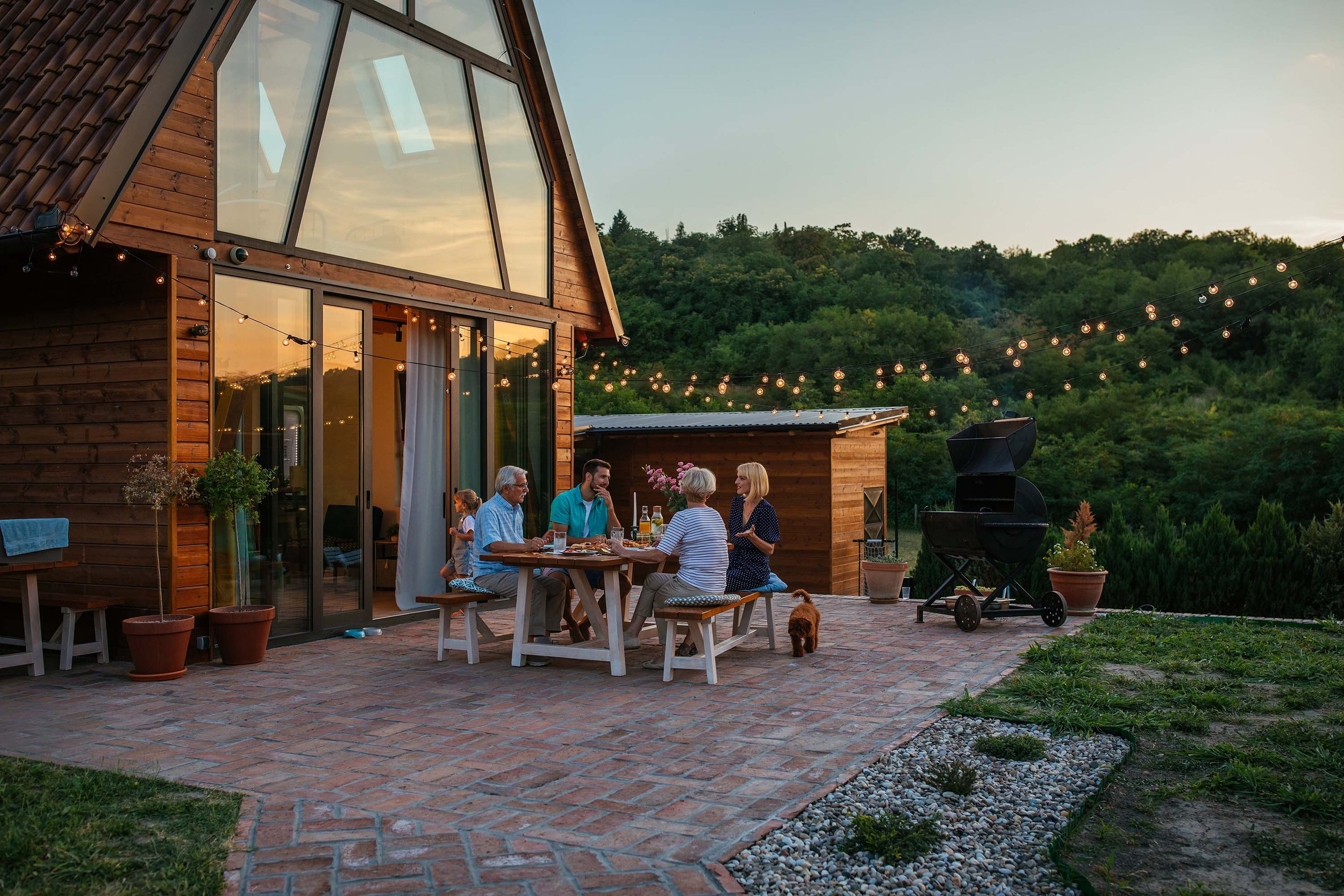 Rustic A-frame cabin with family dining outside under patio lights
