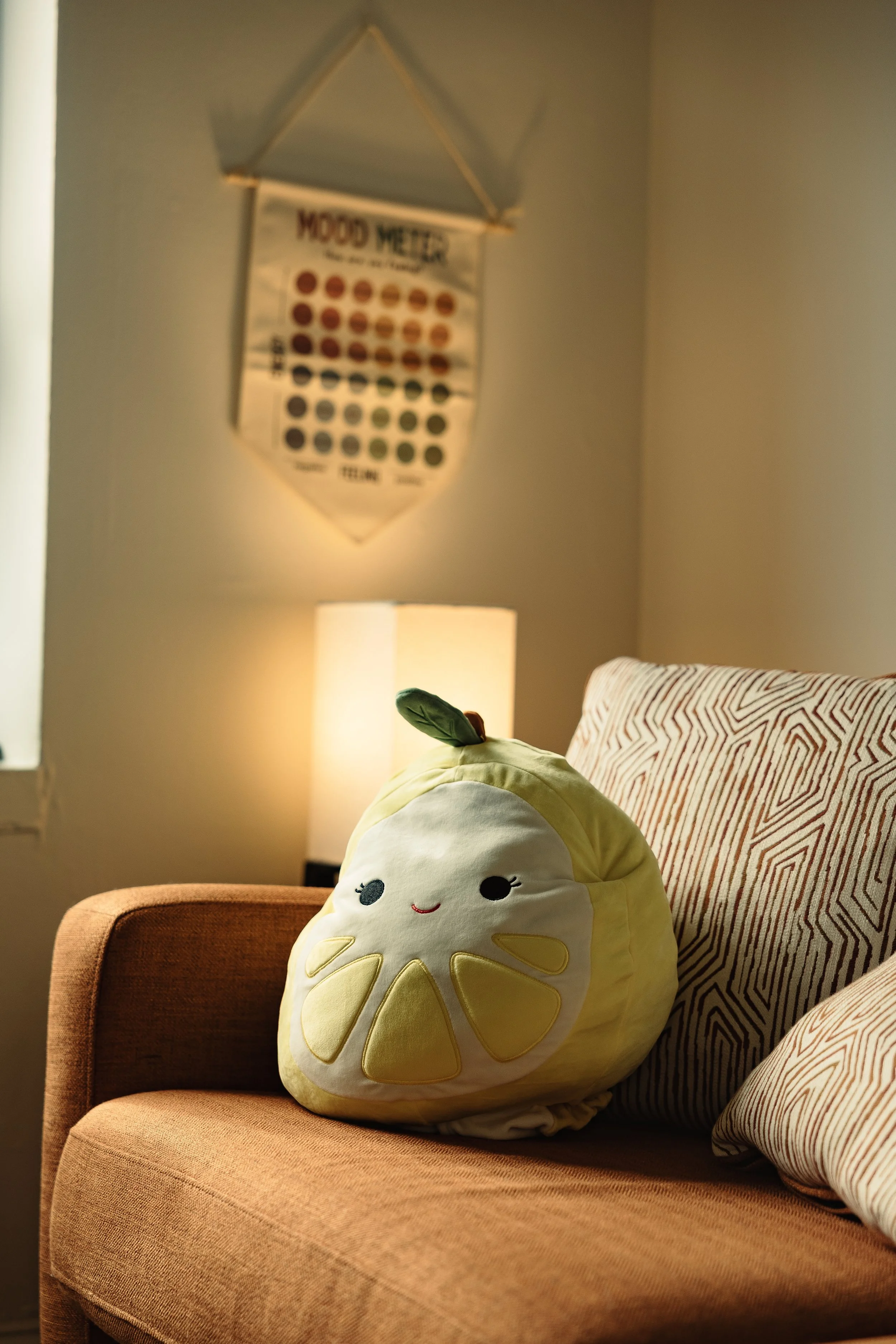 Decorative plush pillow shaped like a cupcake with a smiling face on a brown armchair in a cozy living room.