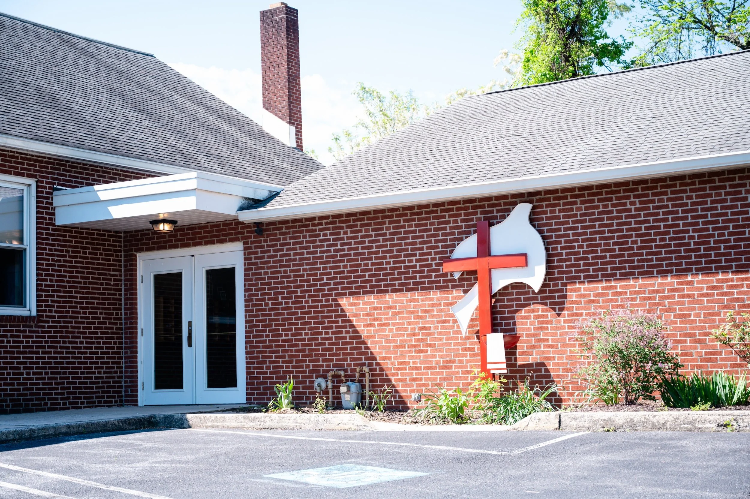 A brick building with a church sign and a parking lot in front, sunny day with clear sky.