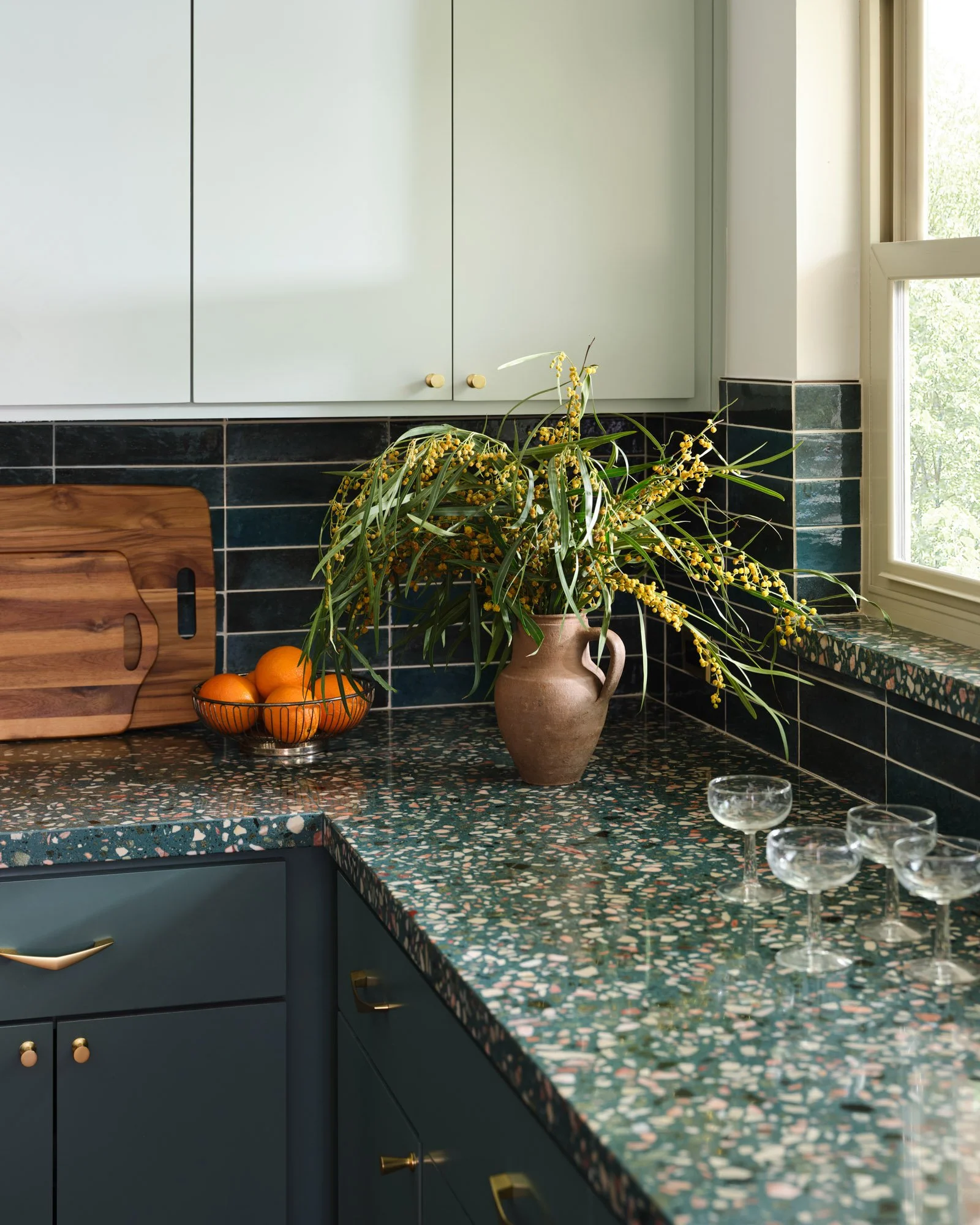 Detail of a Dallas kitchen renovation featuring green terrazzo countertops, dark blue tile backsplash, brass hardware, and deep green cabinetry by Paige Studio.