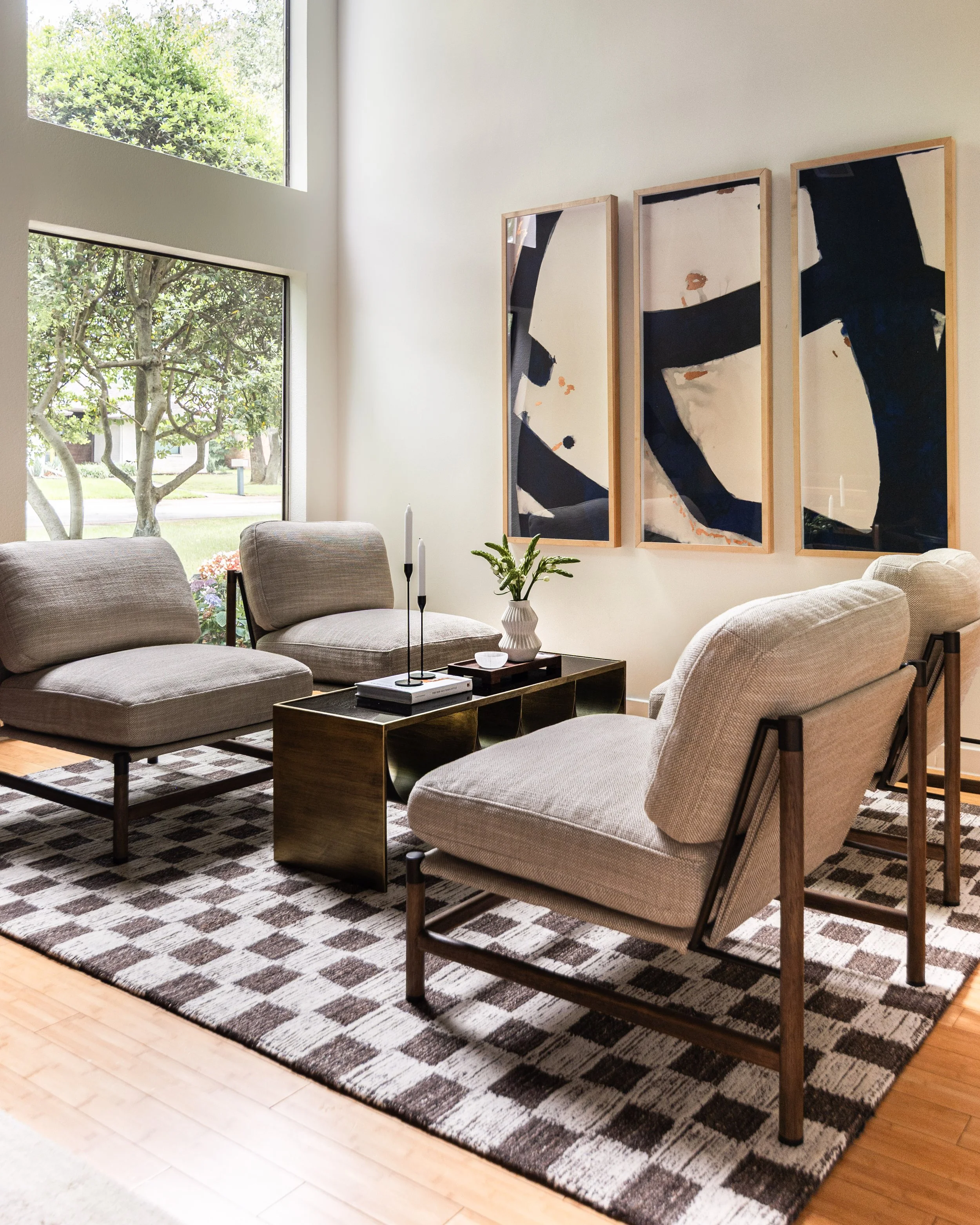 Contemporary Dallas sitting room featuring upholstered lounge chairs, a sculptural bronze coffee table, large abstract artwork, and a geometric patterned rug.
