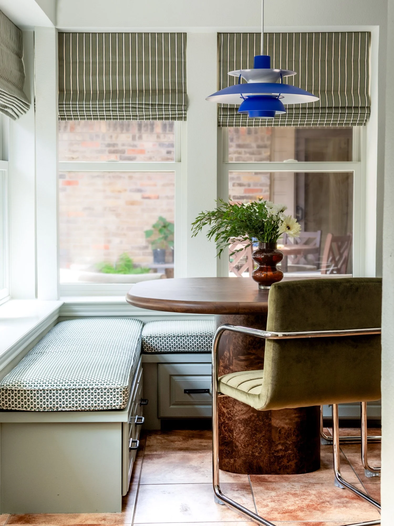 Dallas breakfast nook featuring custom built-in banquette seating, patterned cushions, striped Roman shades, a blue pendant light, and a green velvet chair.