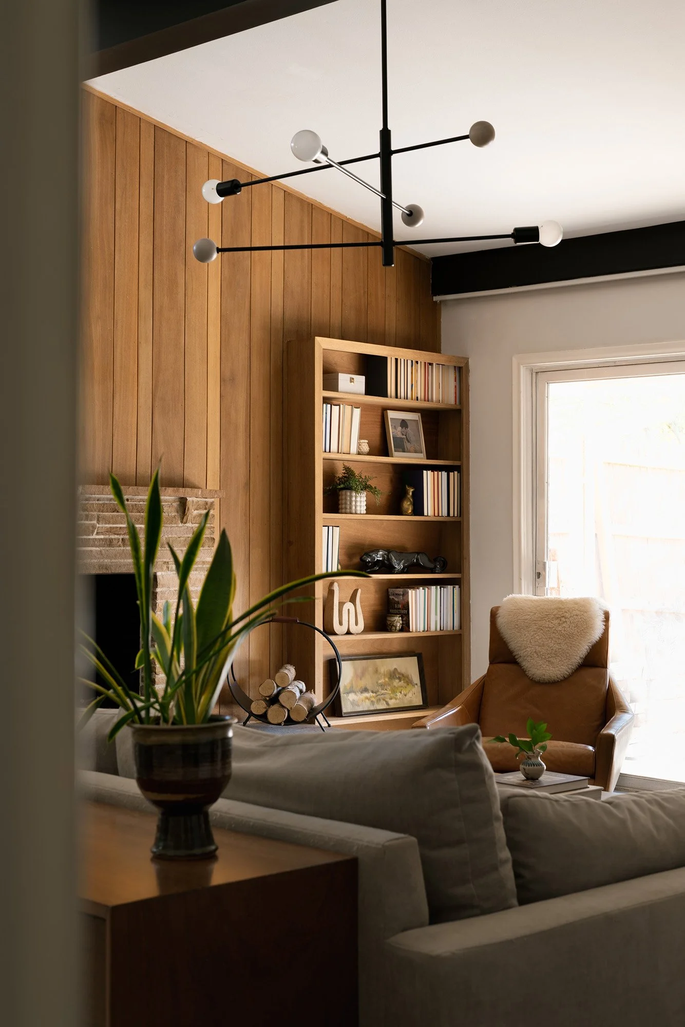 Mid-century modern Dallas living room featuring original wood-paneled walls, a sculptural black chandelier, vintage-style leather lounge chair, and curated furnishings.