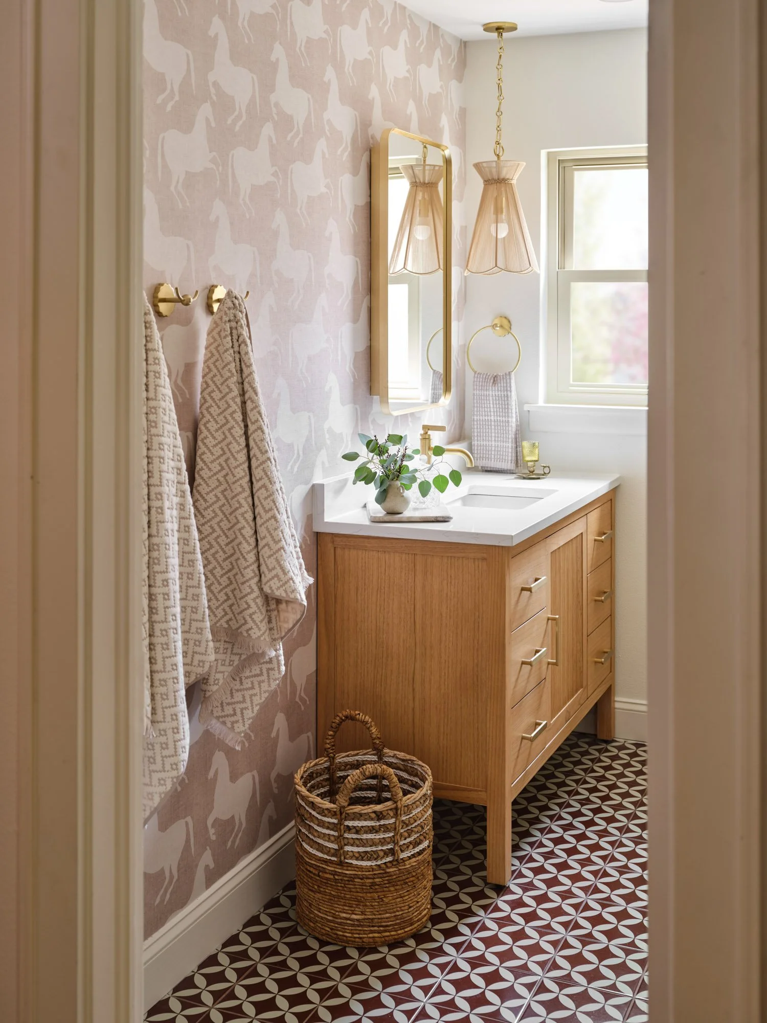 Dallas guest bathroom featuring whimsical horse-patterned wallpaper, a natural wood vanity, brass fixtures, and geometric floor tile designed by Paige Studio.