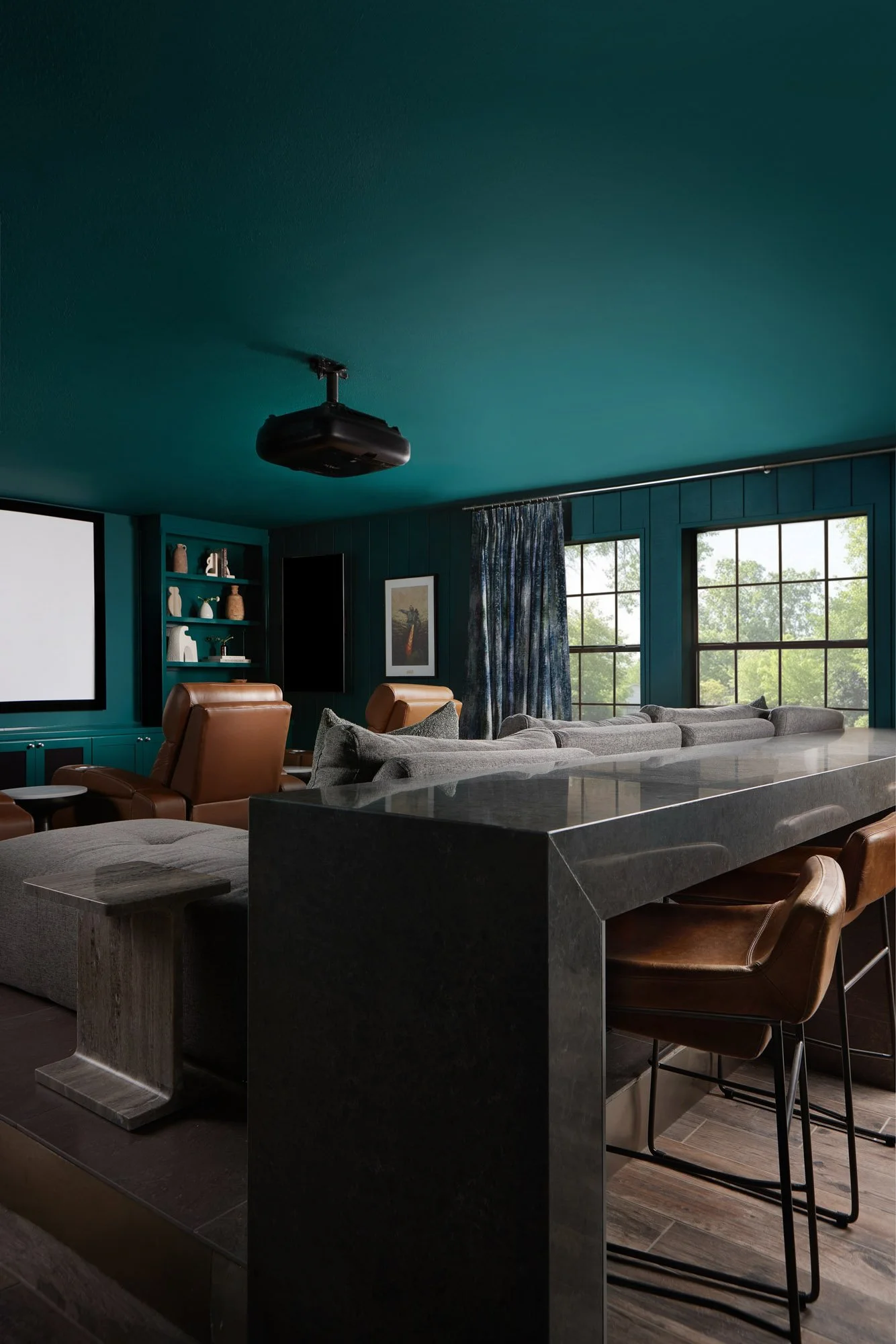 Dallas home theater featuring a custom stone bar with leather barstools, deep teal walls, built-in shelving, and reclining theater seats.