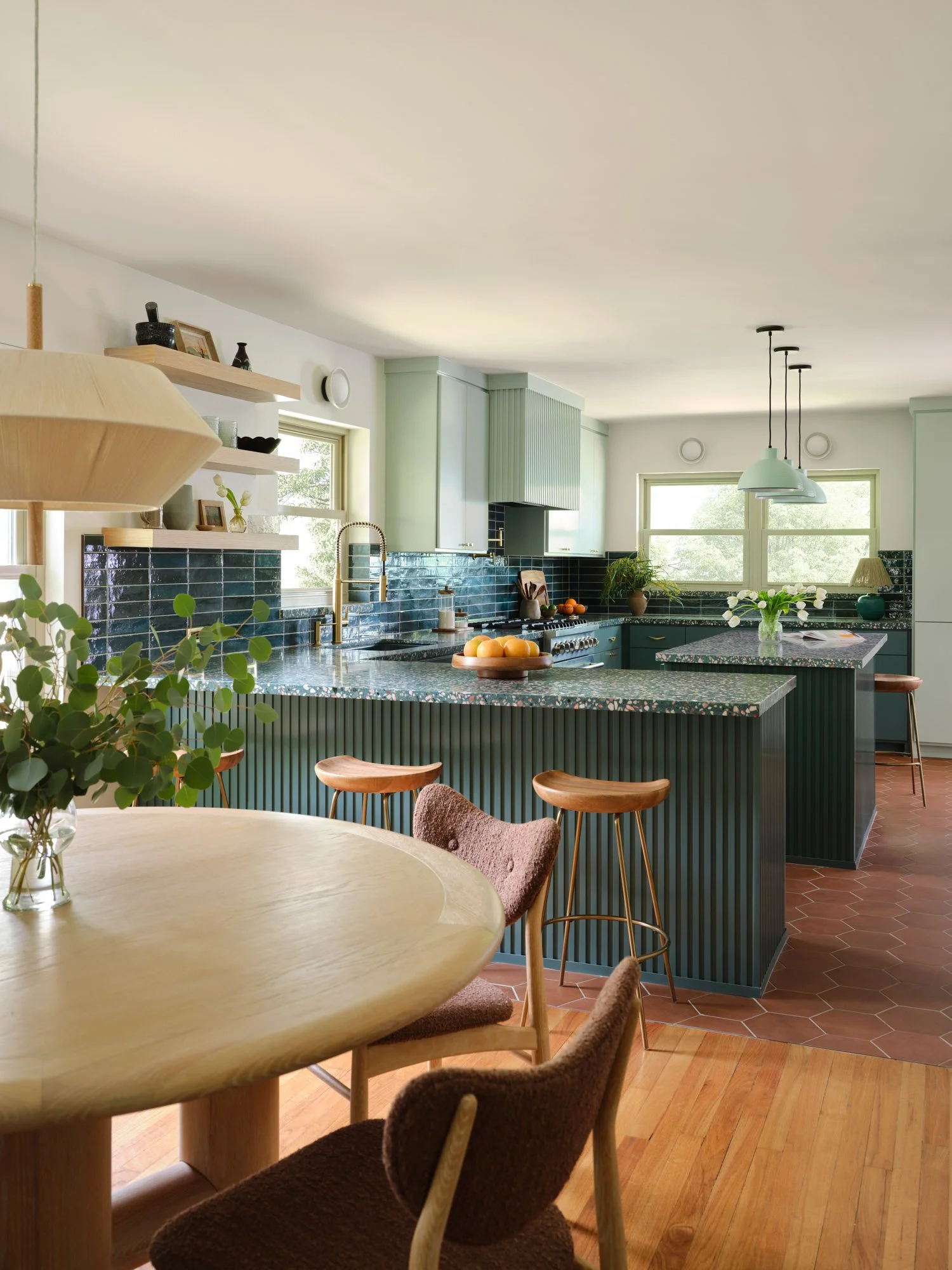 Open-concept Dallas kitchen renovation featuring a fluted green island, terrazzo countertops, blue tile backsplash, and adjoining dining area designed by Paige Studio.