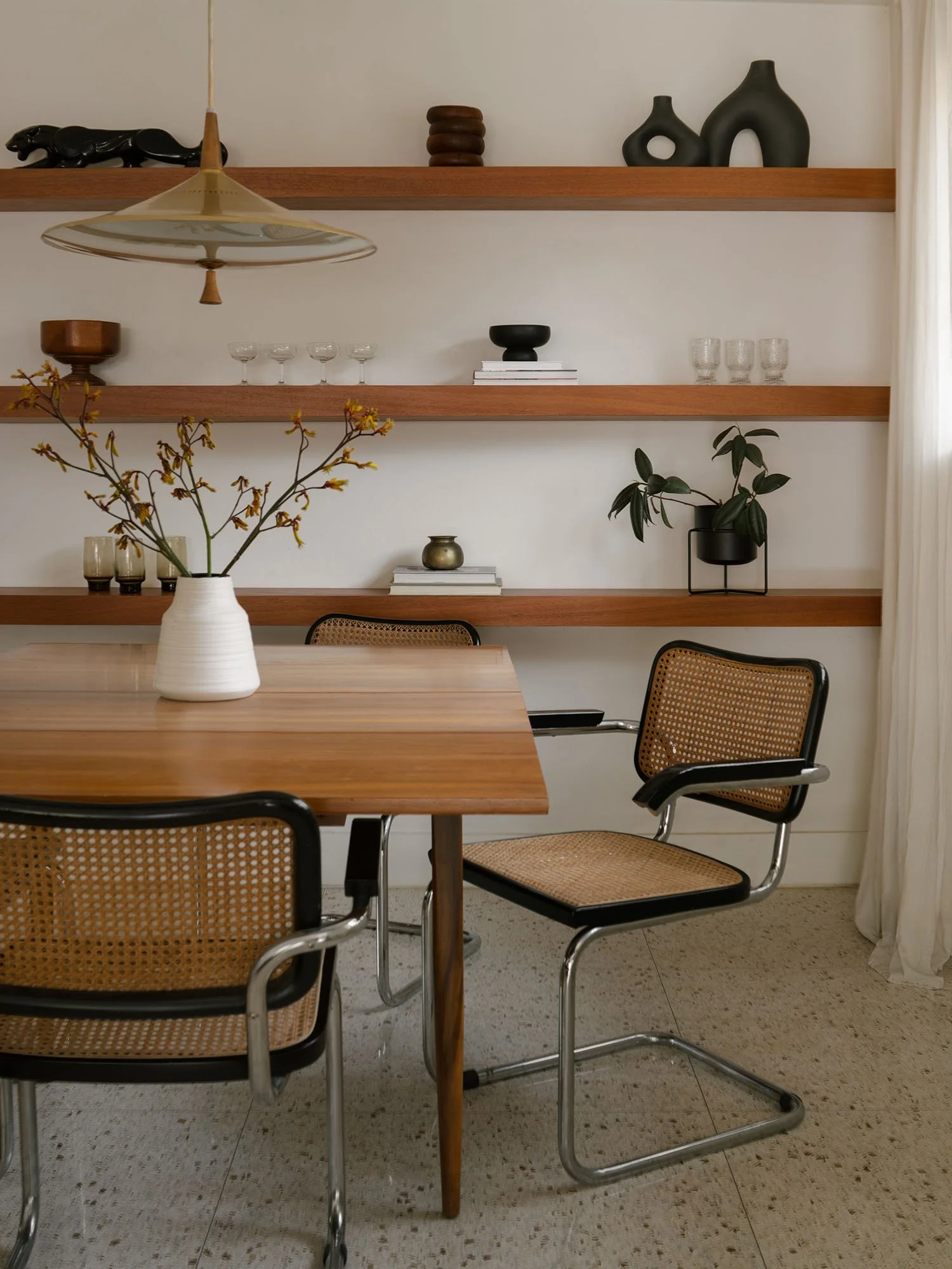 Mid-century modern Dallas dining room featuring authentic vintage Cesca chairs, floating wood shelves, and a sculptural pendant light.