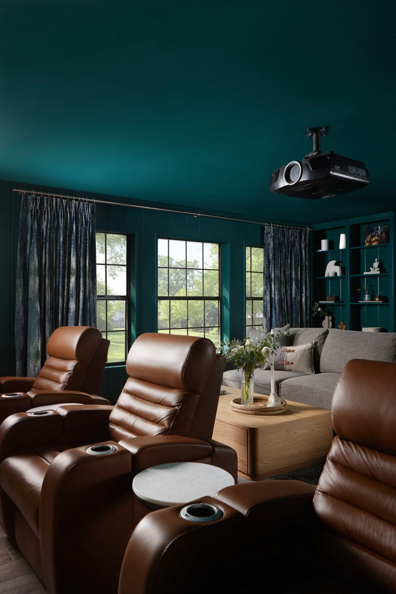 Color-drenched Dallas media room featuring cognac leather reclining theater seats, a gray sectional sofa, teal paneled walls, and custom drapery.
