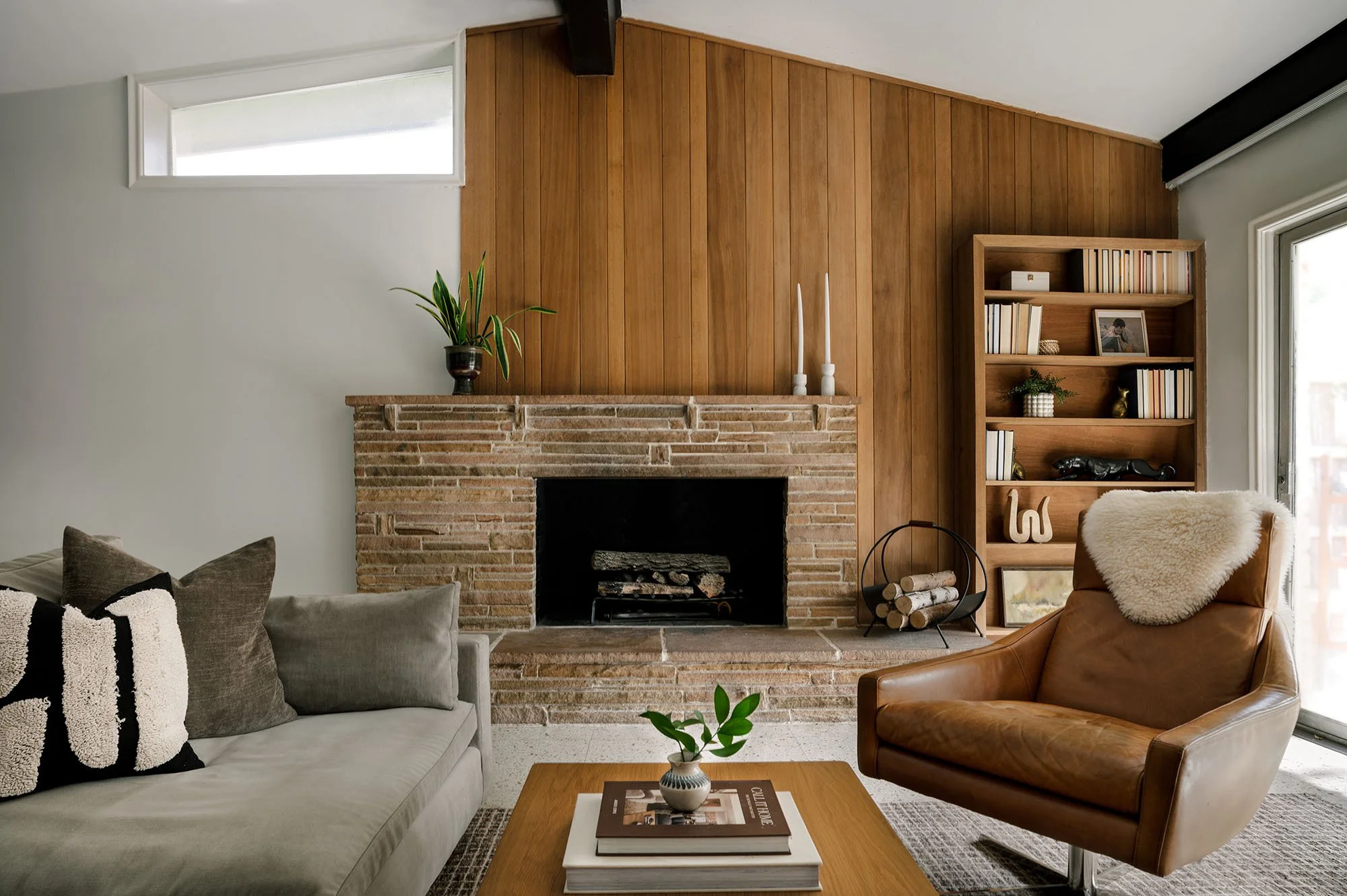 Mid-century modern living room in Dallas featuring original wood-paneled walls, a vintage brick fireplace, a leather lounge chair, and warm wood furnishings.