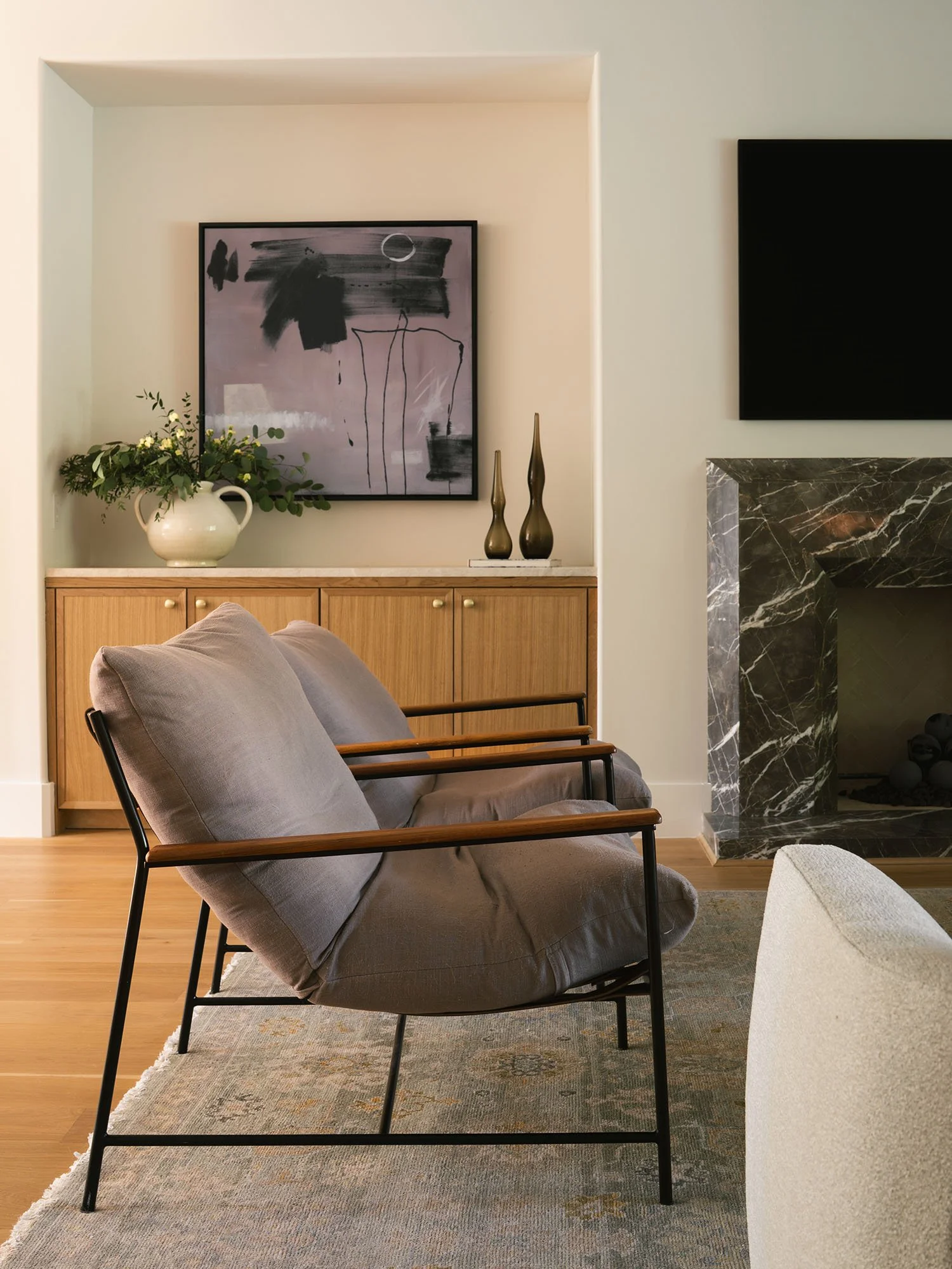Contemporary living room featuring a sculptural lounge chair, custom wood cabinetry, abstract artwork, and a dramatic stone fireplace.
