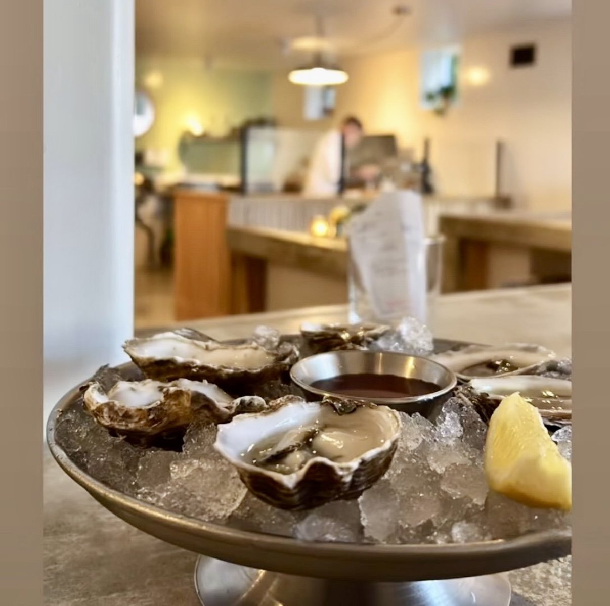 Oysters on a bed of ice with lemon wedge and dipping sauce in a restaurant setting.