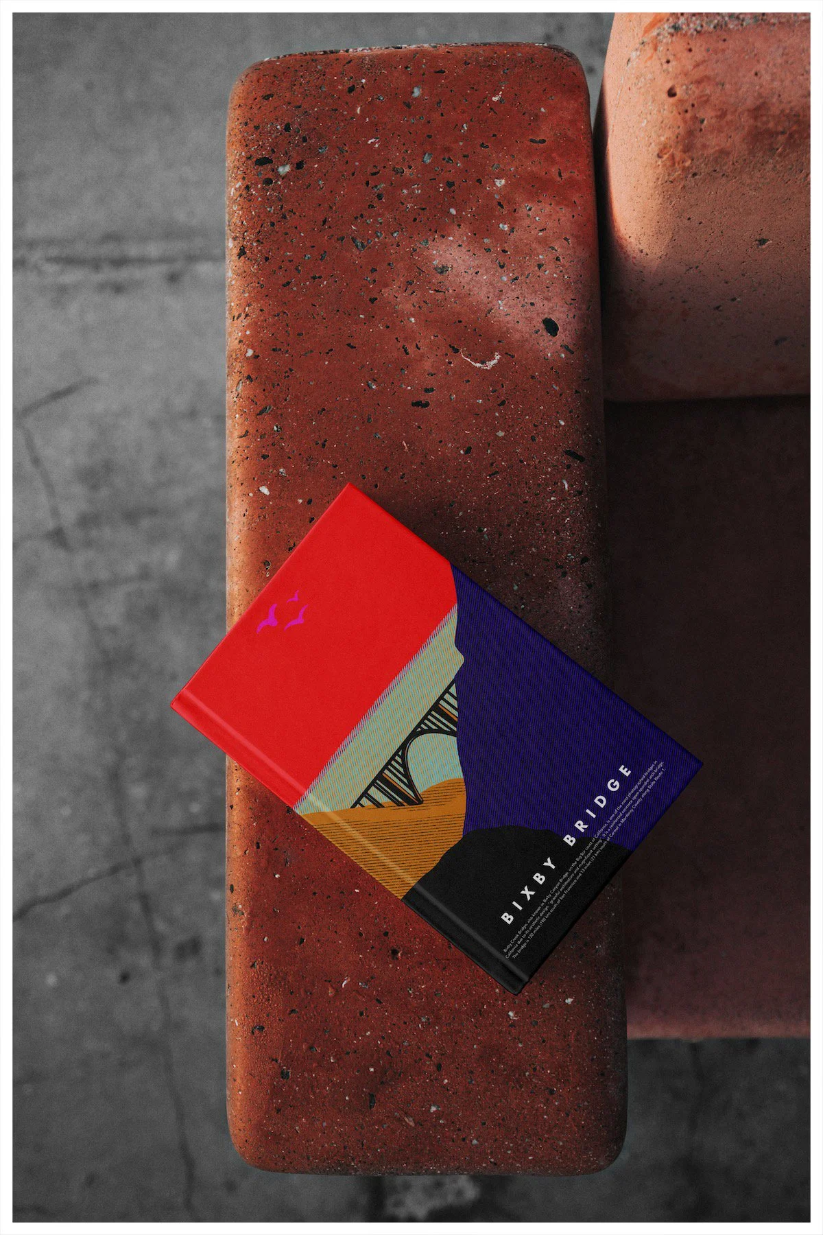 A book mockup using a design showcasing the location of Bixby Bridge in Big Sur, California with a minimalism approach. Poster design by Carmelo Rossette.