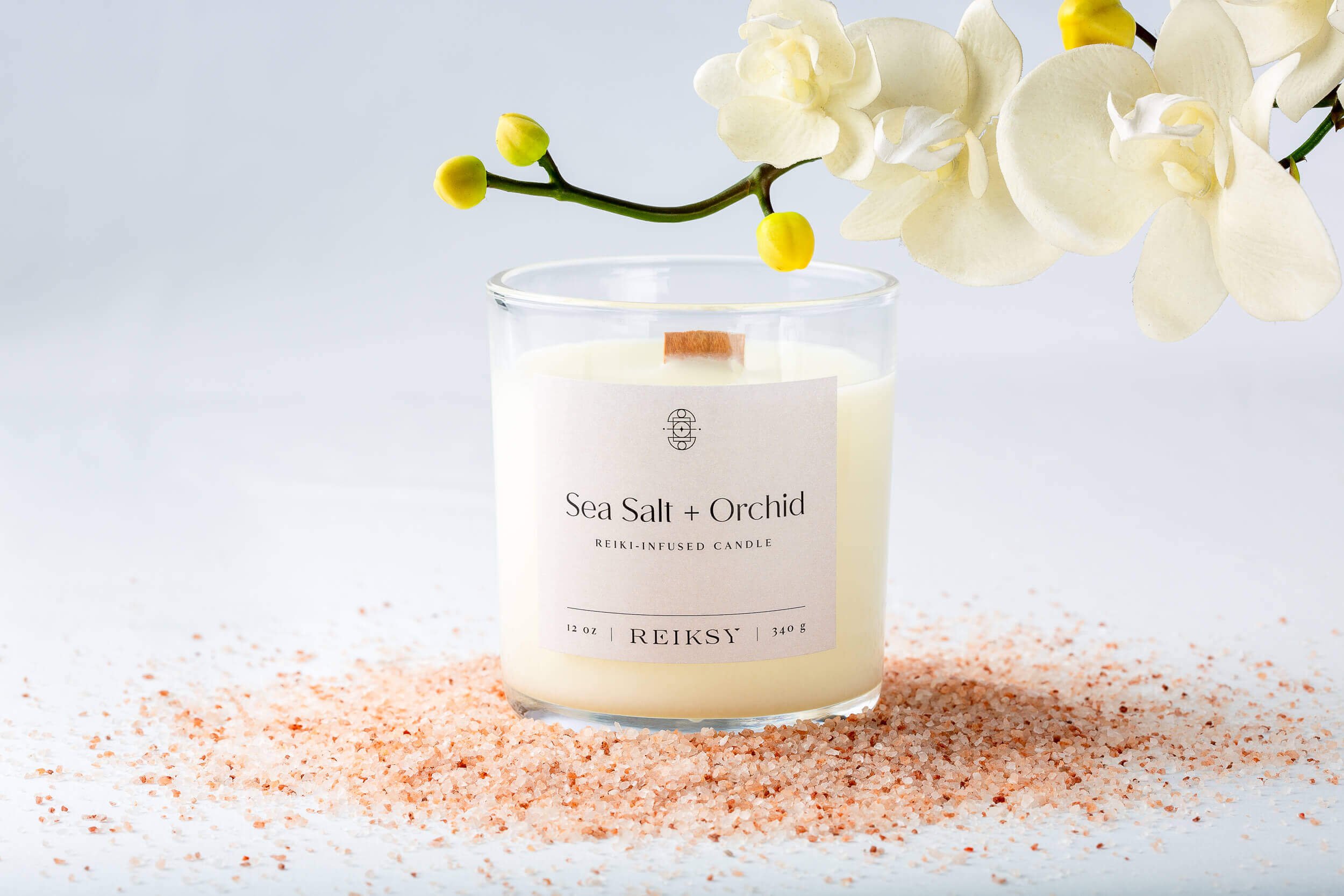 Sea salt and orchid Reiksy reiki-infused candle surrounded by a Himalayan sea salt as a white orchid floats above.