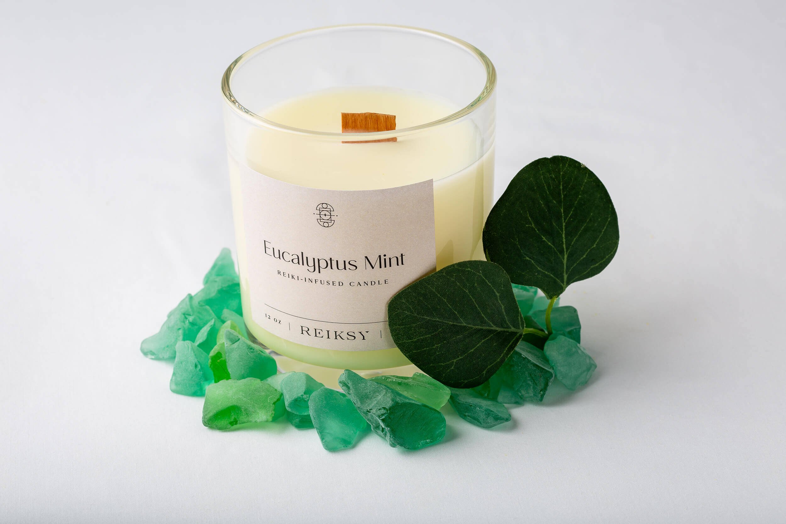 Eucalyptus mint Reiksy reiki-infused candle surrounded by green stones and a mint leaf..