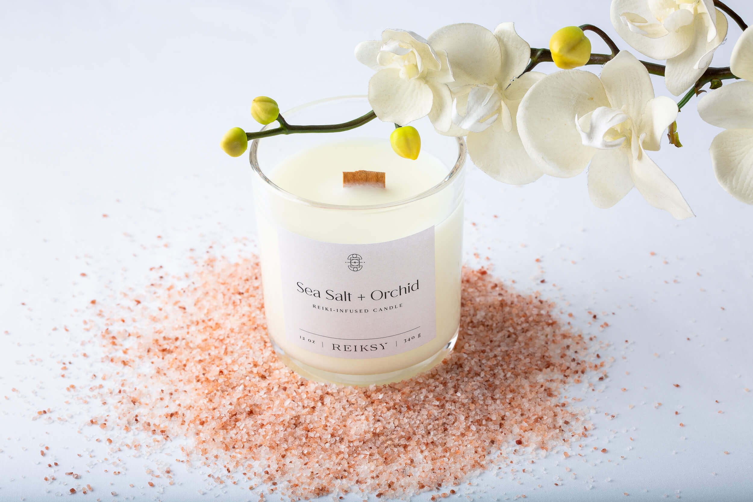 Sea salt and orchid Reiksy reiki-infused candle surrounded by a Himalayan sea salt as a white orchid floats above.