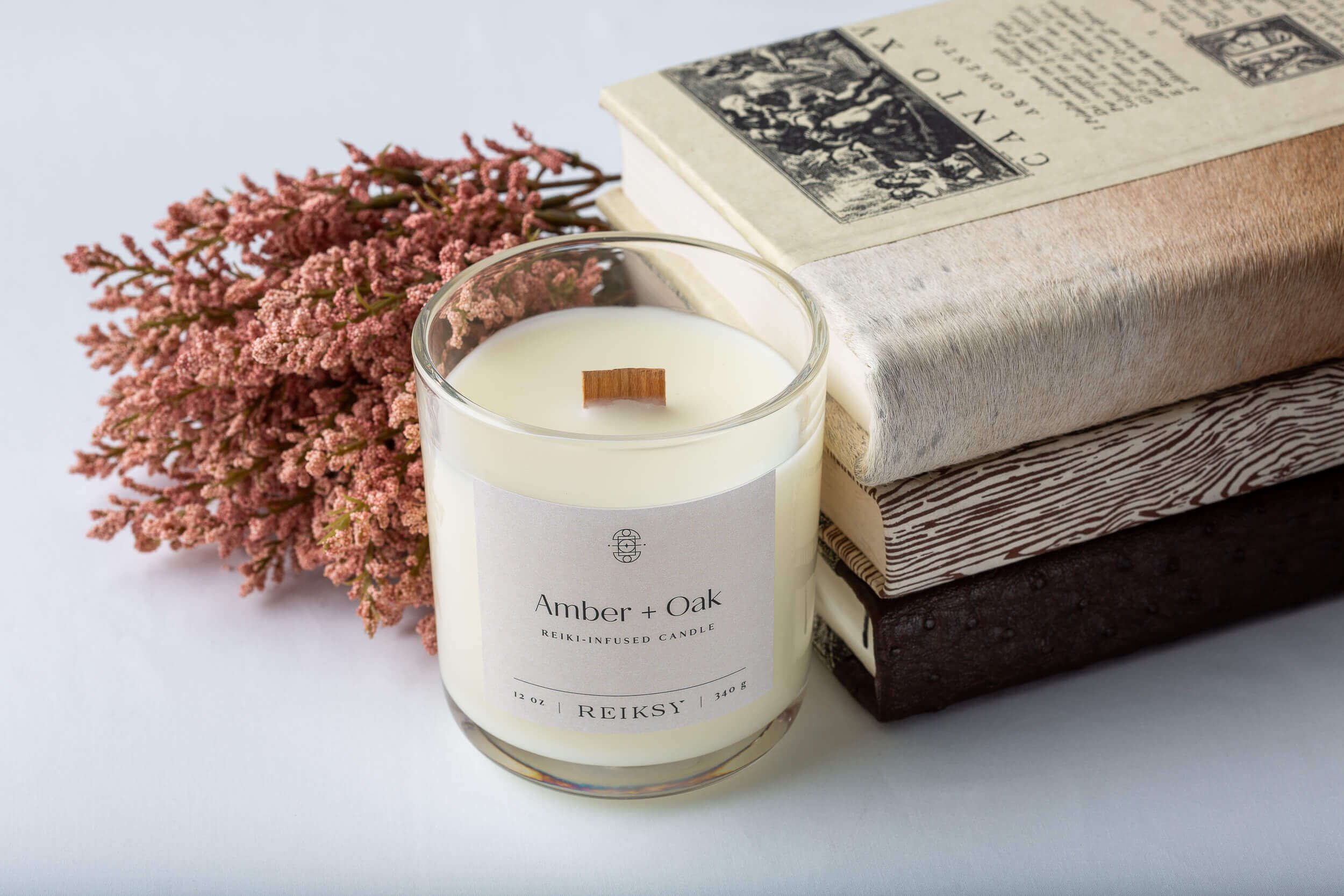 Amber and oak Reiksy reiki-infused candle with books and peach-colored flowers.