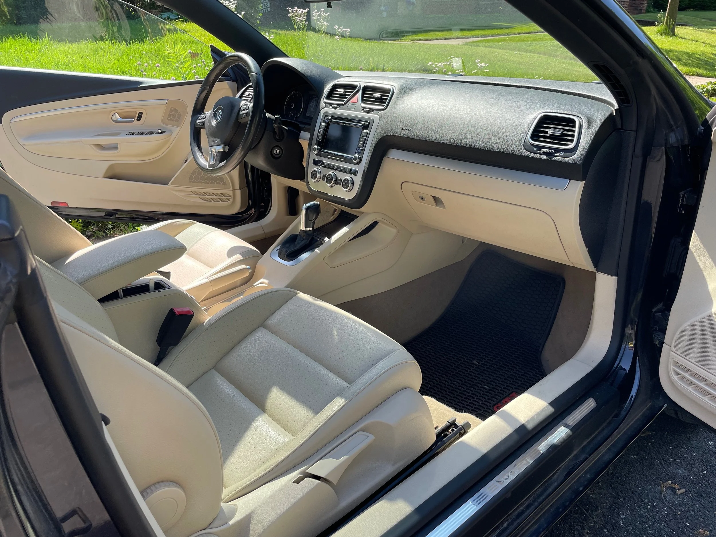 Interior of a Volkswagen car showing beige seats, black dashboard, steering wheel, center console with gear shift, and front passenger side floor mat.