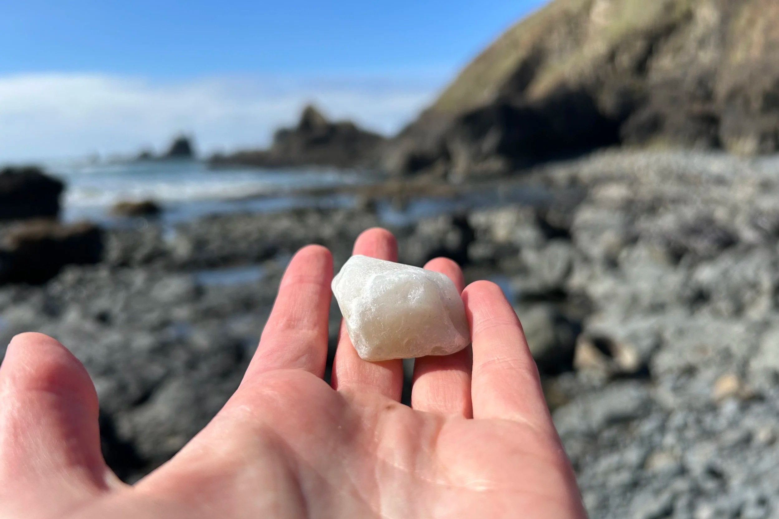 Large white agate on hand with rocky beach in background