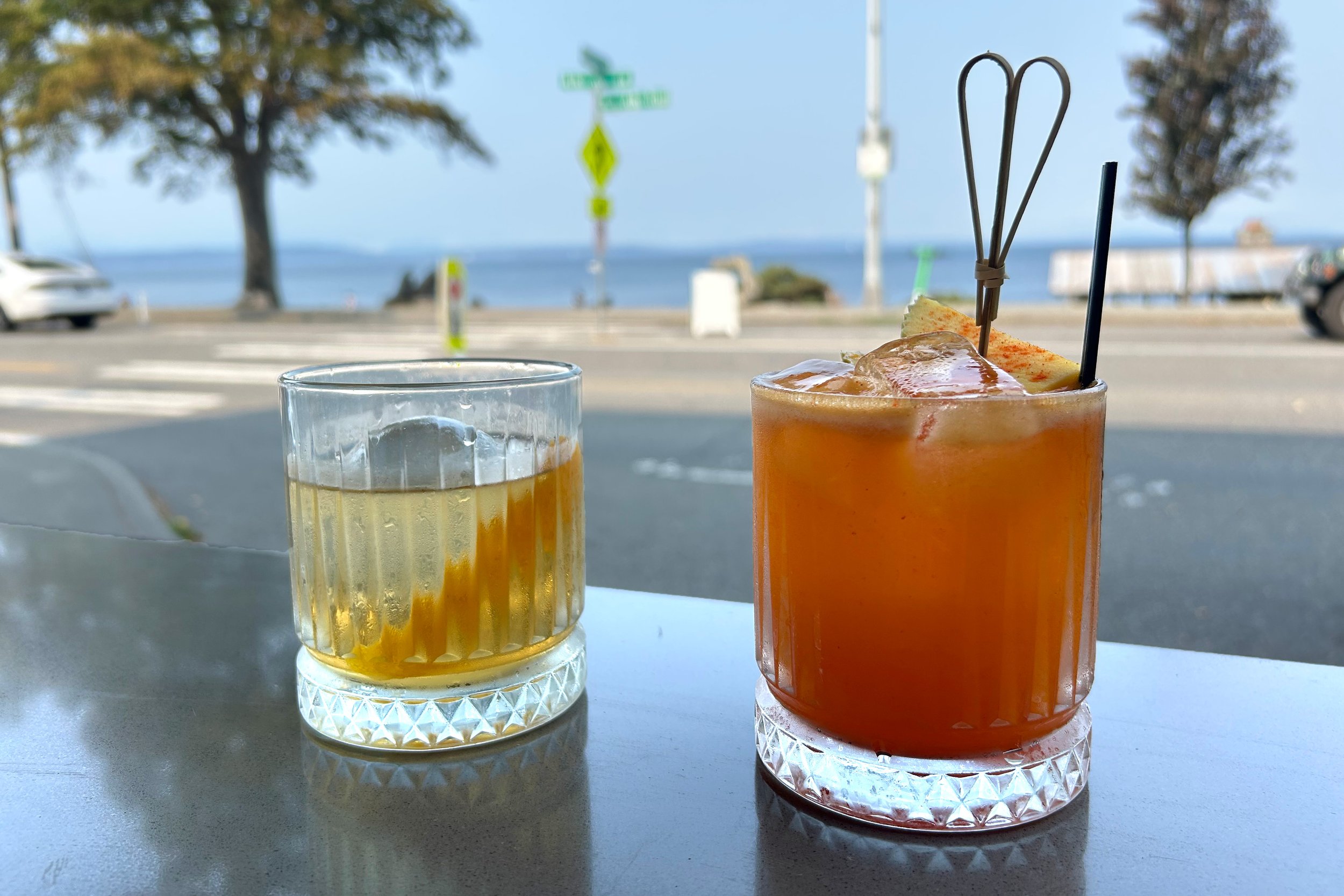 Two cocktails on sidewalk bar with view of Puget Sound