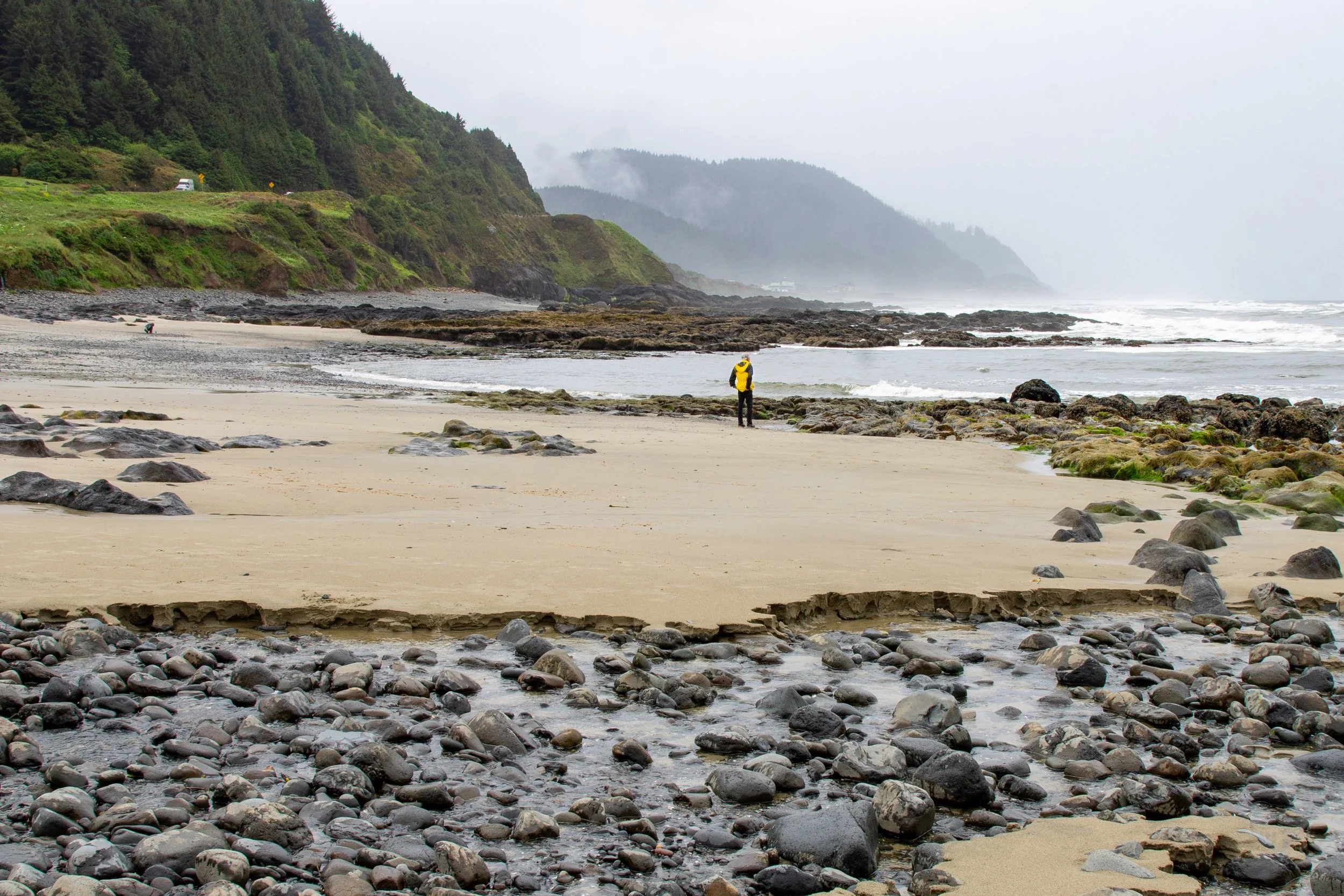 Man stands on beach and looks at foggy hills on Oregon Coast