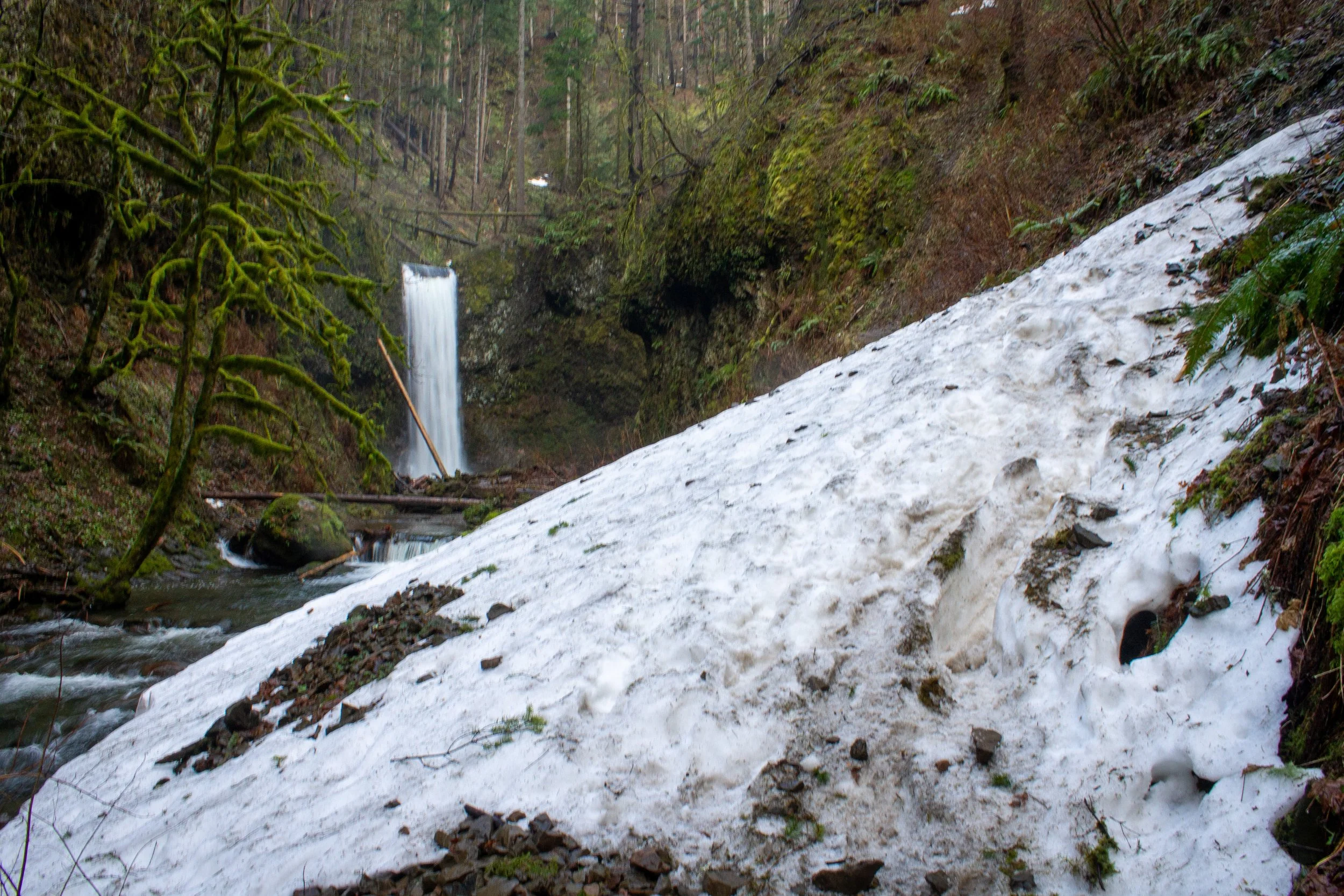 Pile of melting snow on trail in front of waterfall