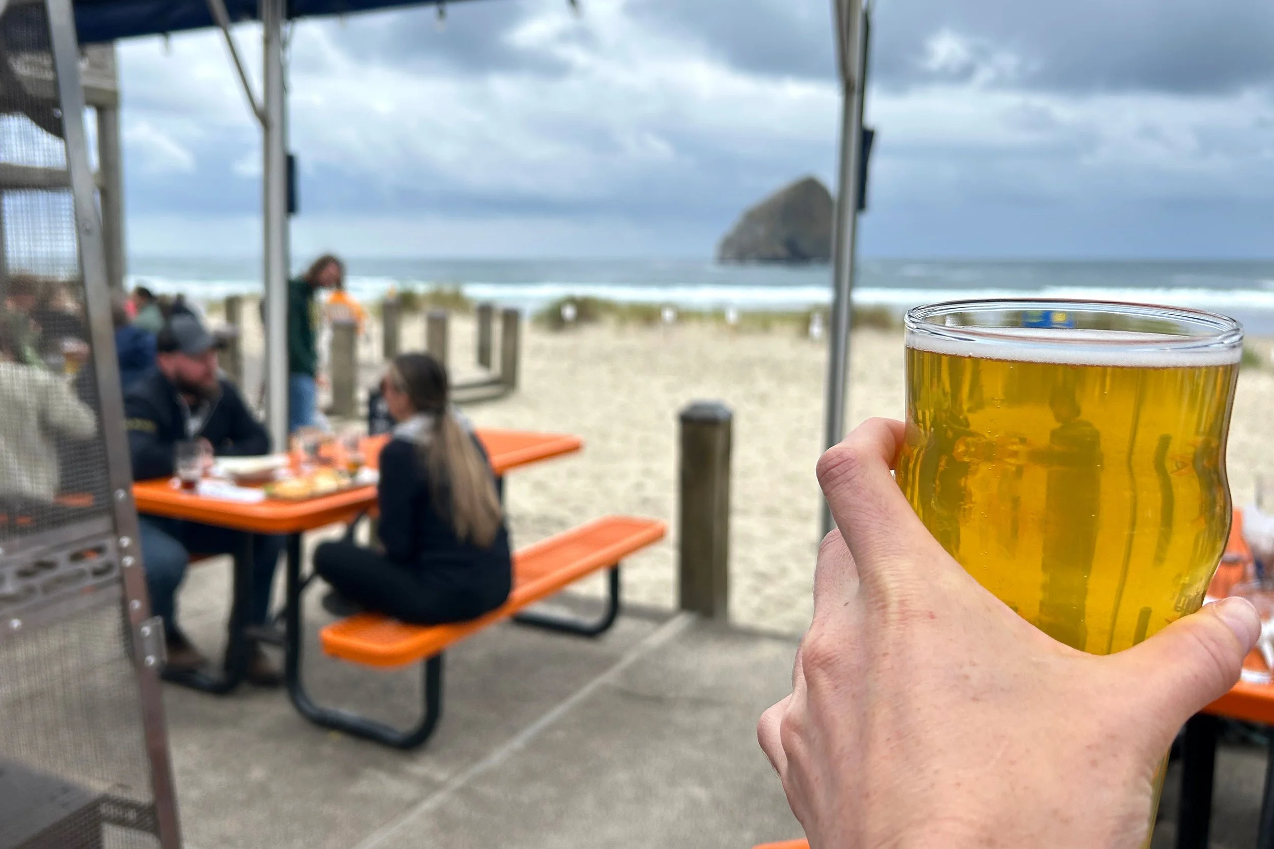 Hand holding a beer in front of Haystack Rock view