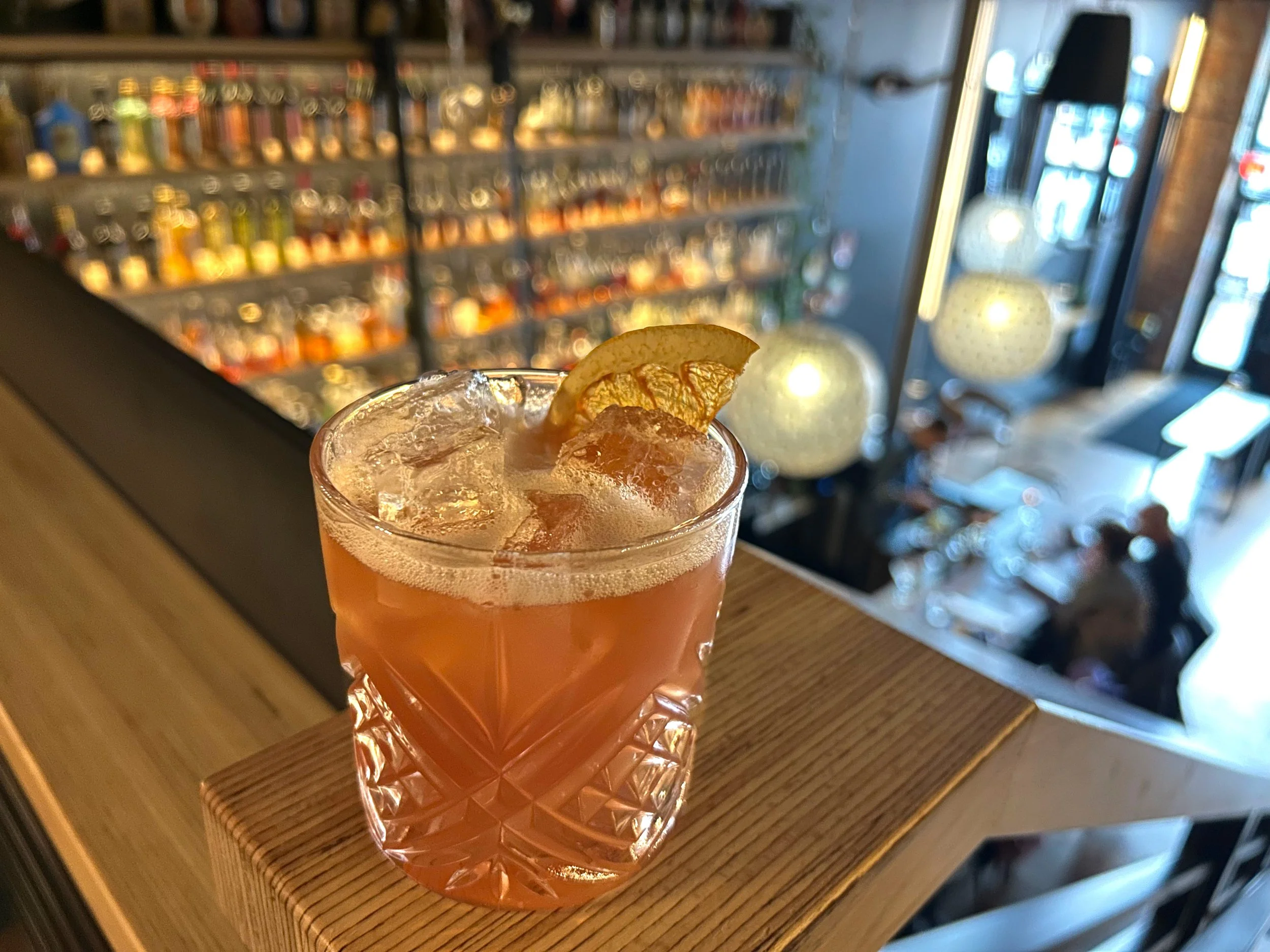 Cocktail with candied orange slice garnish on railing in Bar RBC