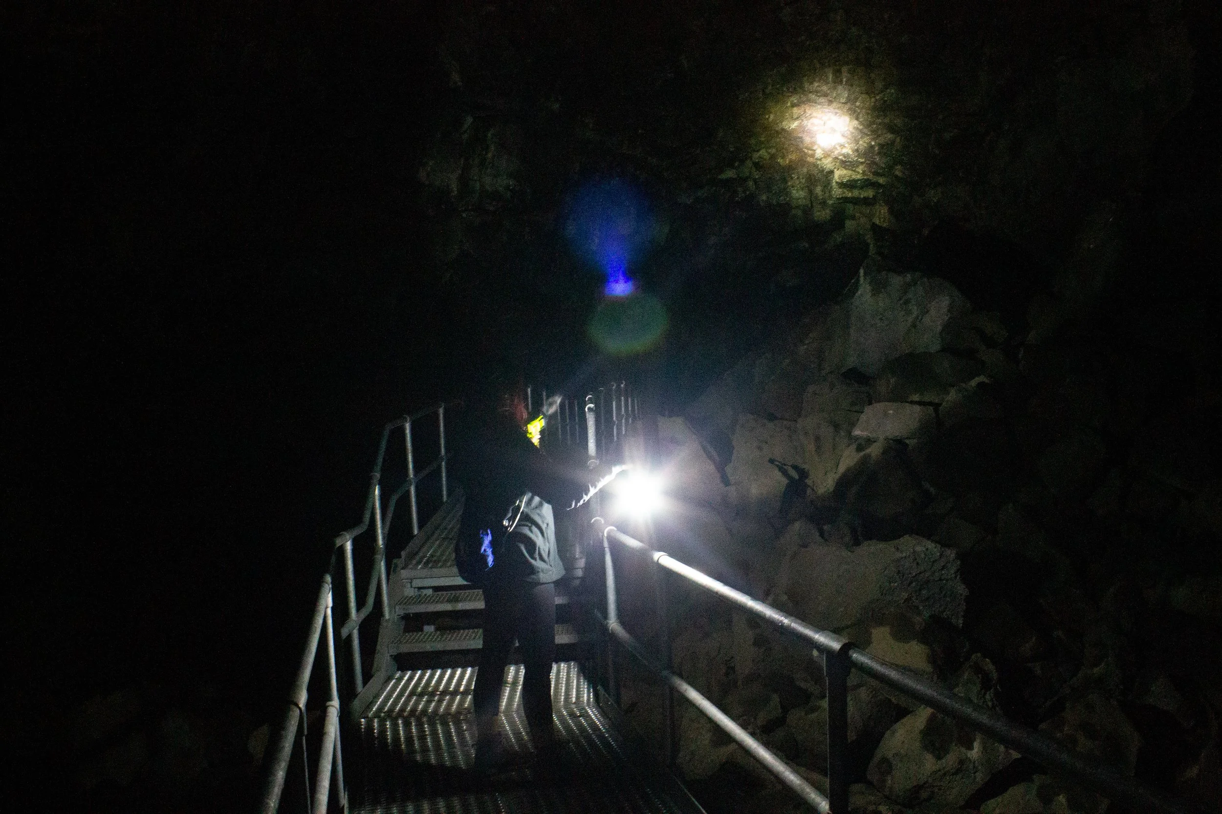 Person on metal walkway in cave holds lantern and flashlight