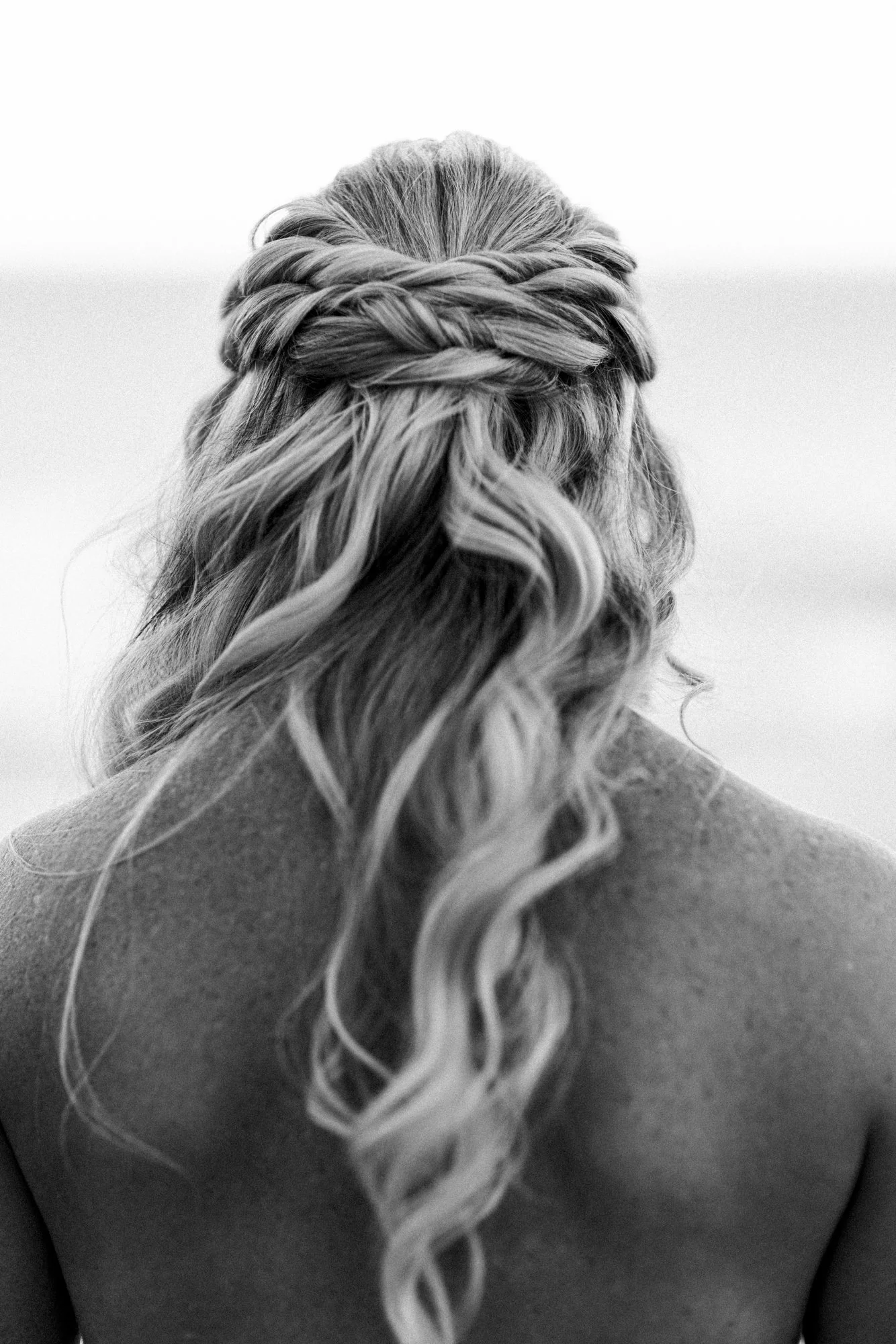 Back view of a woman with wavy hair styled with a braid across the top, in black and white.
