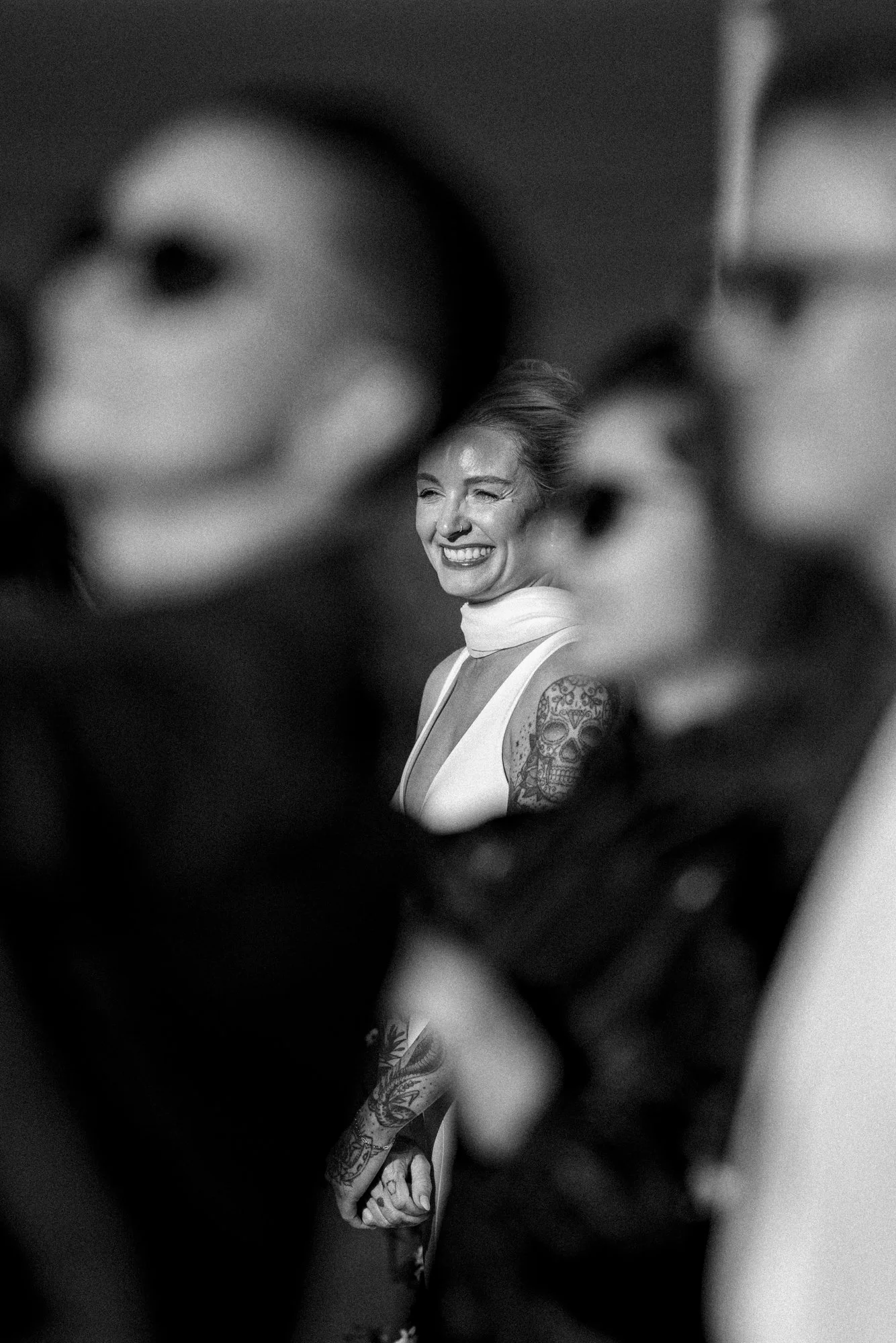 A woman with tattoos smiling and looking through two masks in the foreground.